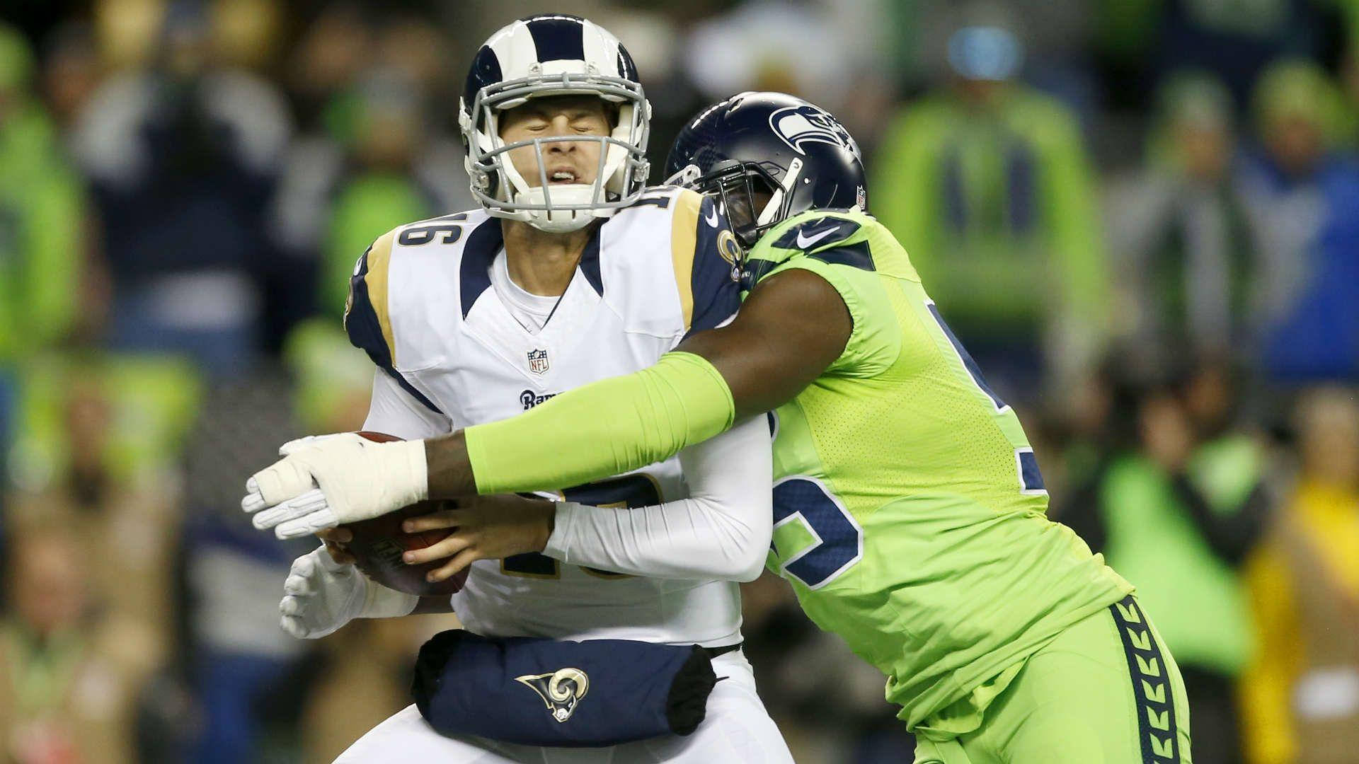 賈瑞德·高夫NFL 2019 壁紙 — 一名身穿白色球衣的美式足球四分衛在夜間比賽中，在體育場燈光下被一名亮綠色防守球員擒抱。
