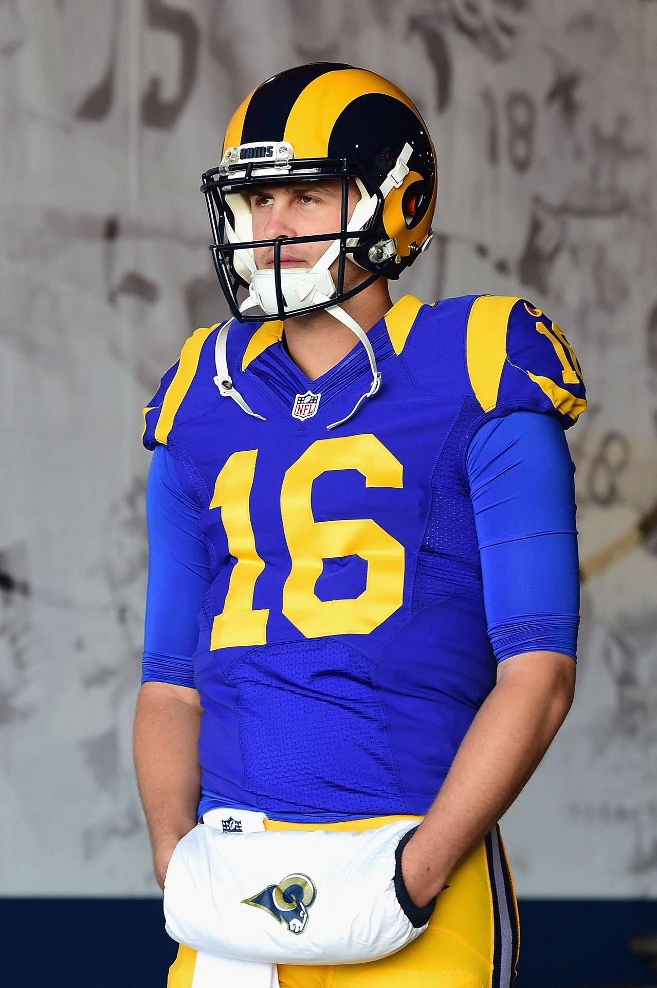 賈瑞德·高夫足球運動員 壁紙 — 一位專注的NFL四分衛身穿藍金色公羊隊16號球衣，站在體育館通道中。