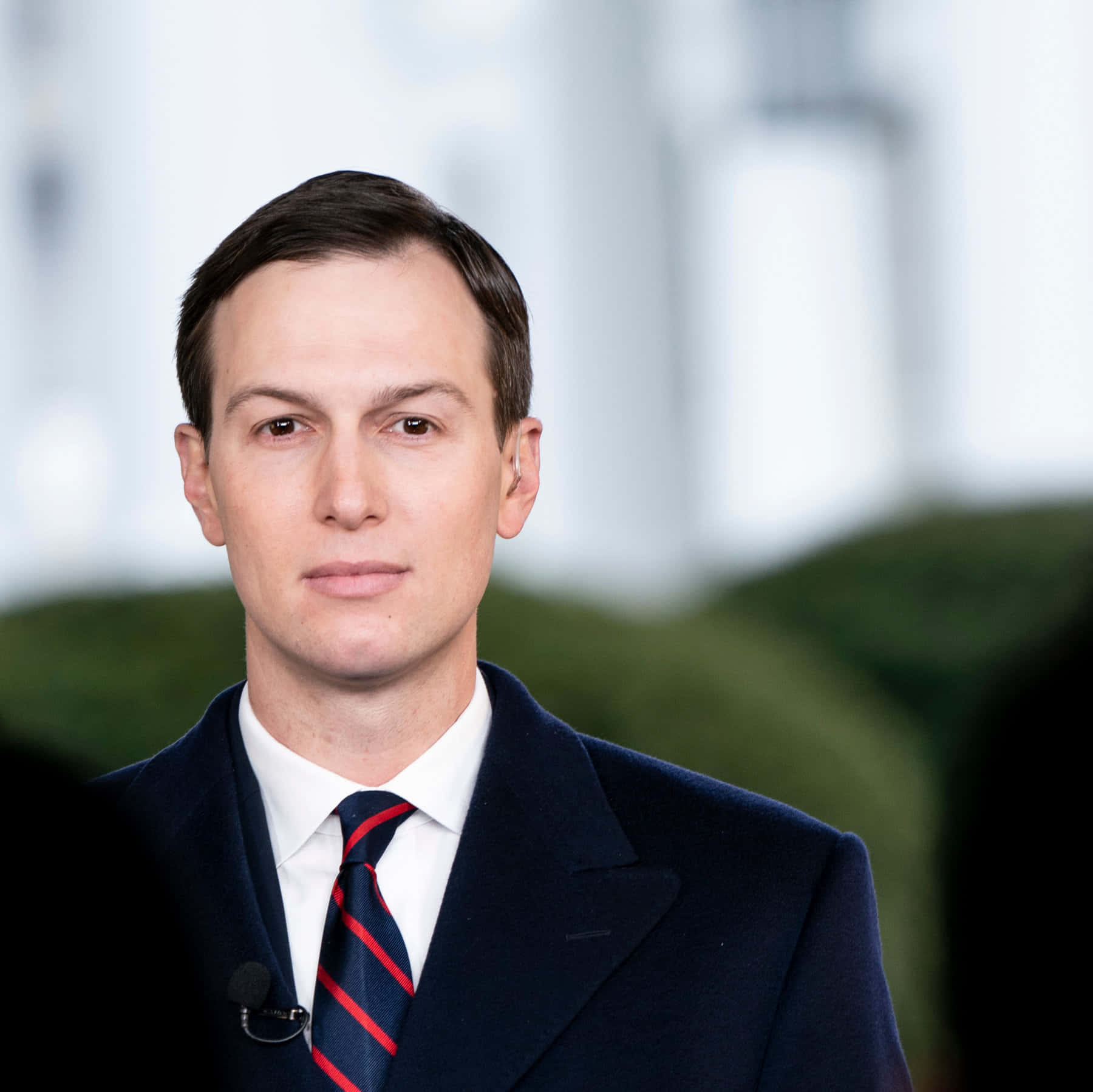 一名身穿深色西裝和紅色條紋領帶的男子直視鏡頭。