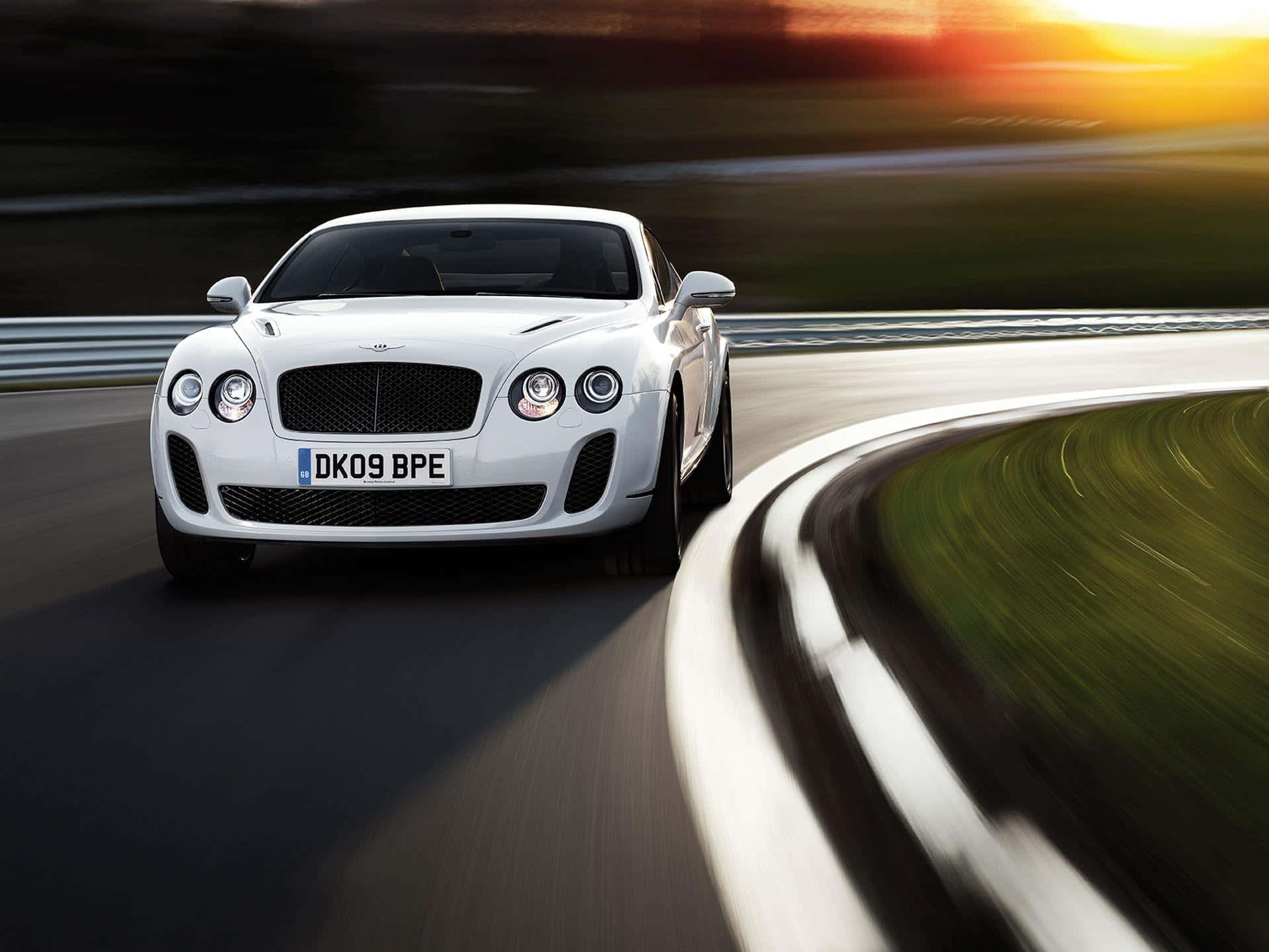 賓利Super Sports 壁紙 — 一輛白色賓利 Continental GT 在日落時分沿著蜿蜒的道路疾馳，動態模糊強調了速度。