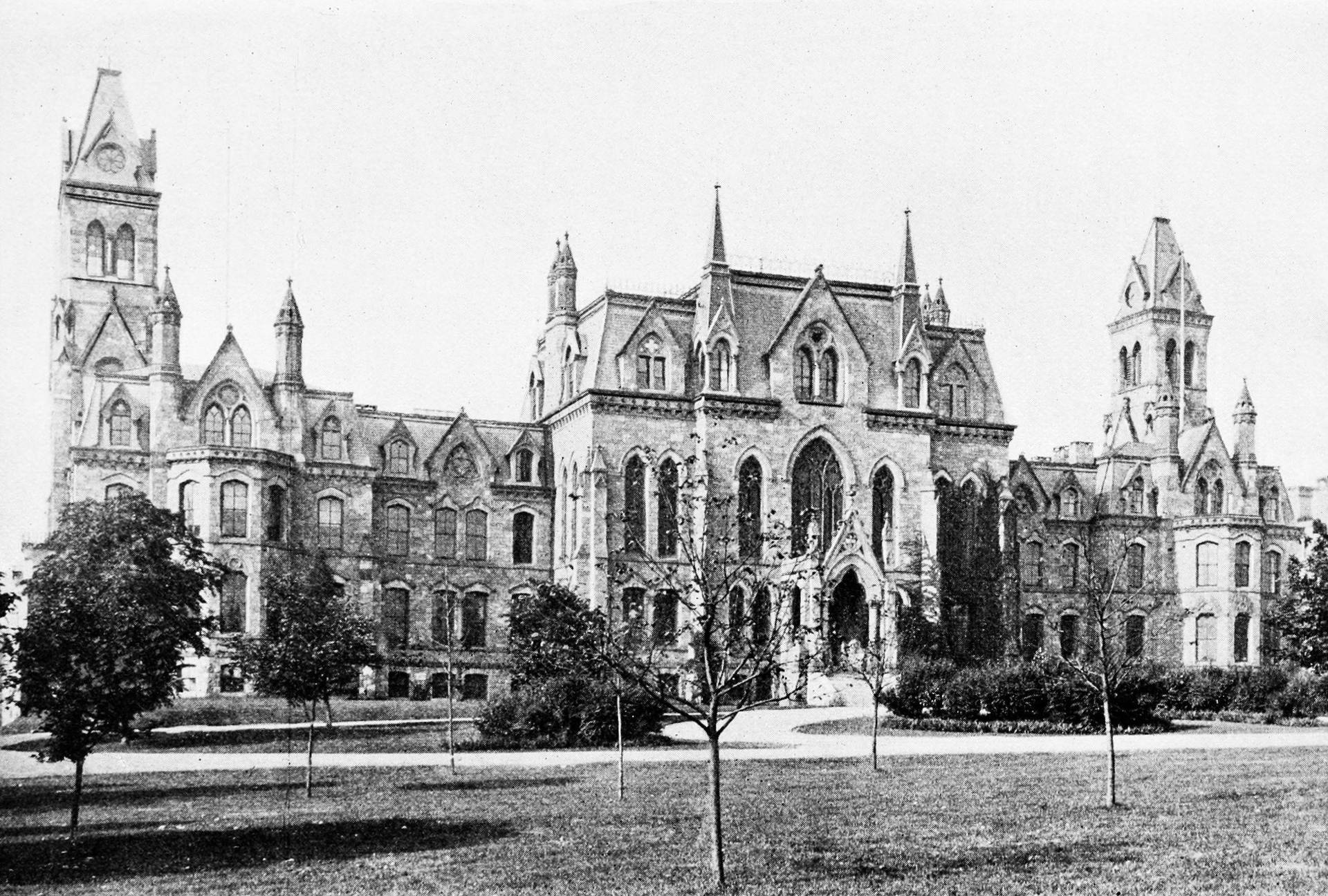 歷史悠久的哥德式大學建築，擁有石塔和拱形窗戶，周圍環繞著樹木和草地。
