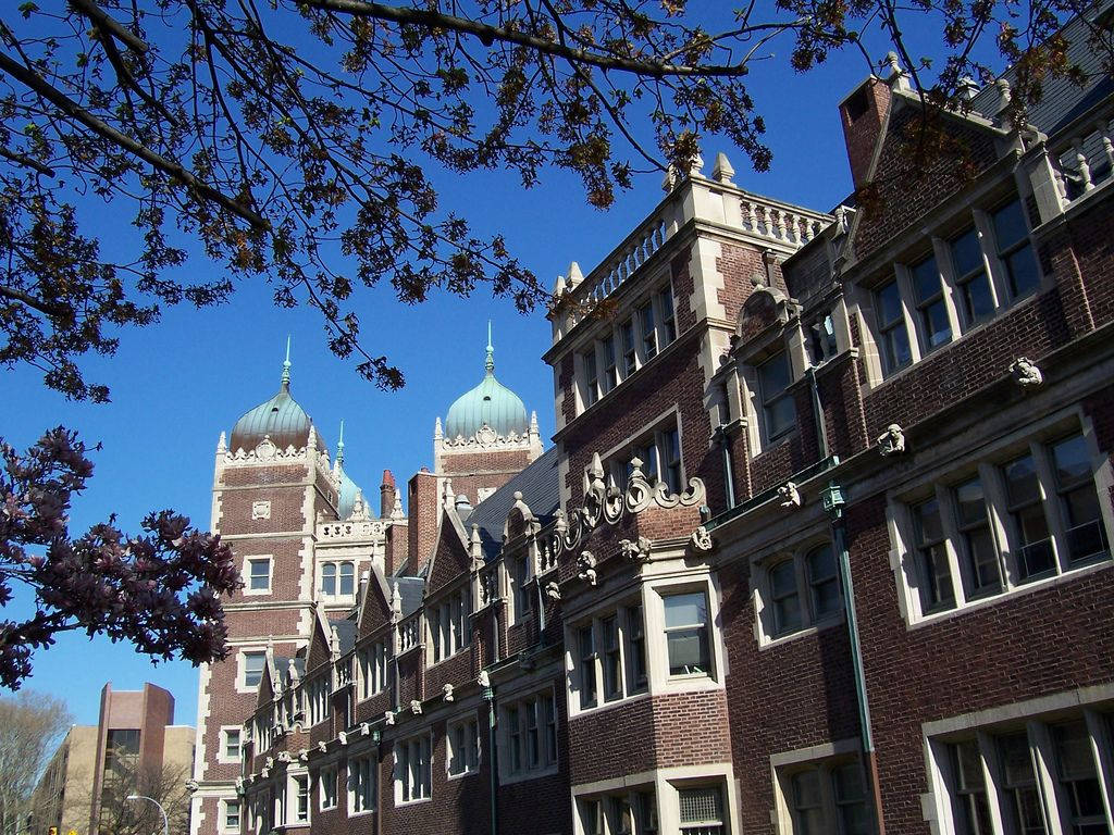 歷史悠久的磚造大學建築，綠色圓頂在清澈的藍天下，被萌芽的樹木環繞。