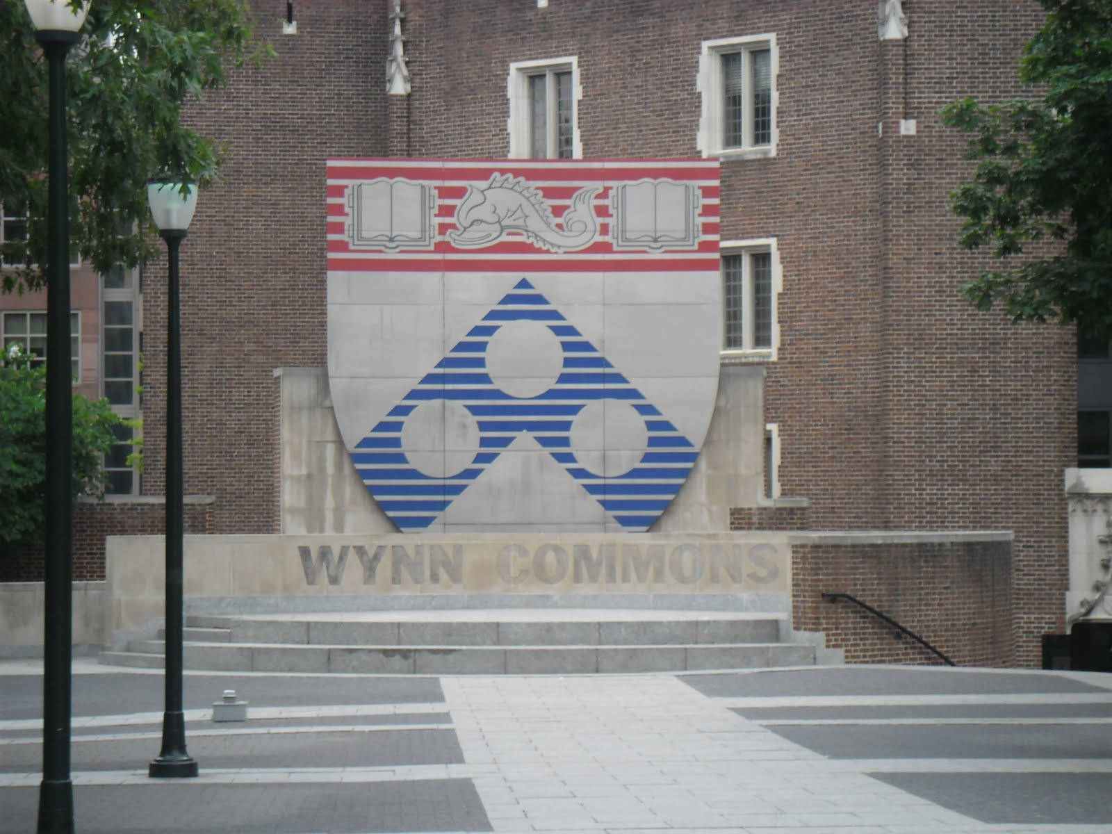 大學校園紀念碑，帶有盾牌和打開的書本，位於磚砌建築前。