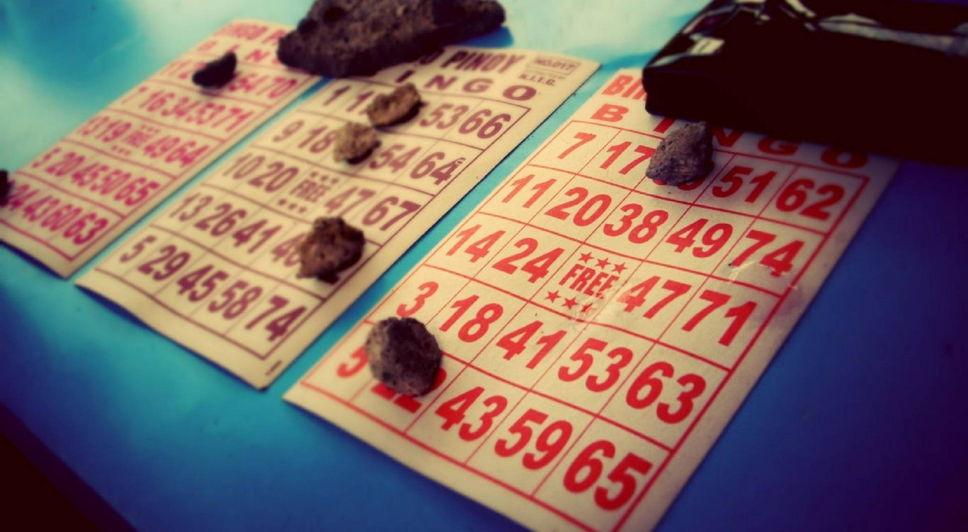 賓果卡與石頭 壁紙 — 藍色表面上放置了紅色數字和深色石頭的復古賓果卡特寫。