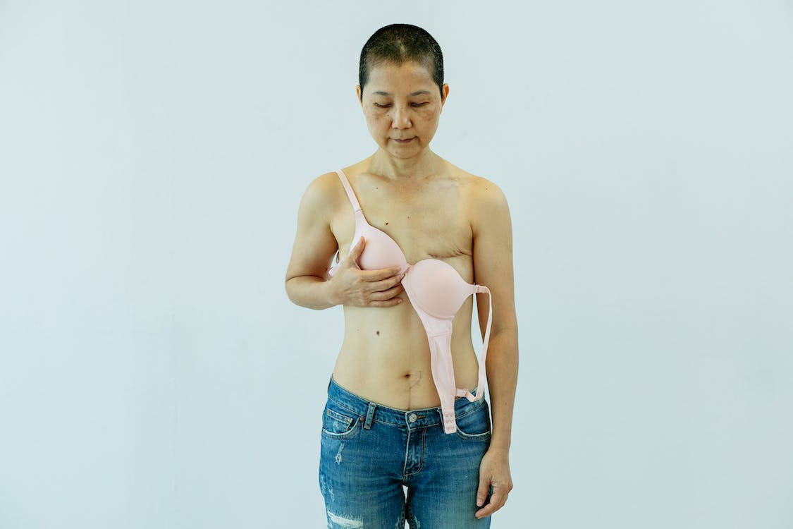 一位穿著牛仔褲的女性在純灰色背景前拿著粉色胸罩。