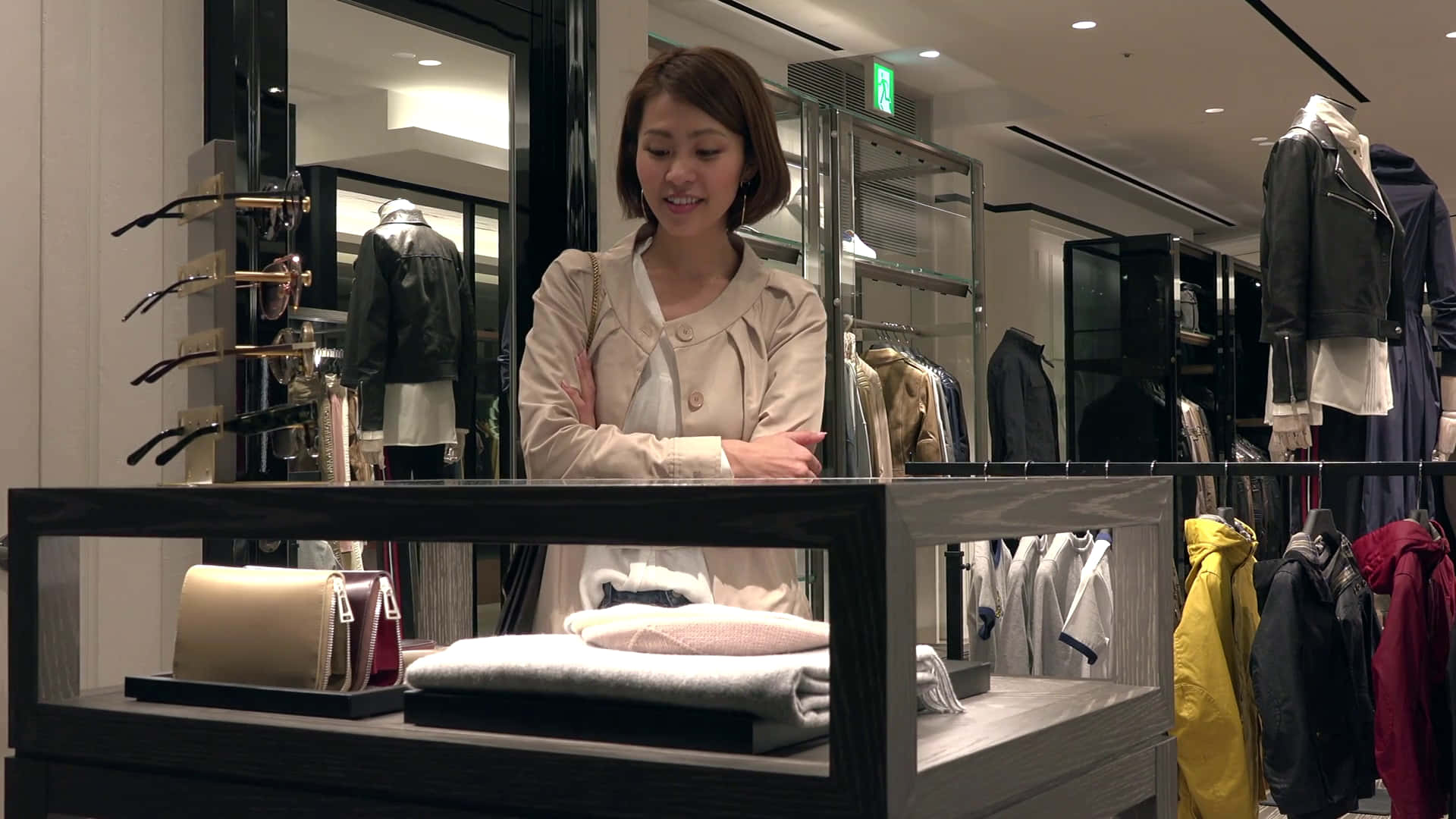 女性在服裝店展示櫃後微笑，櫃內有毛衣和手提包。