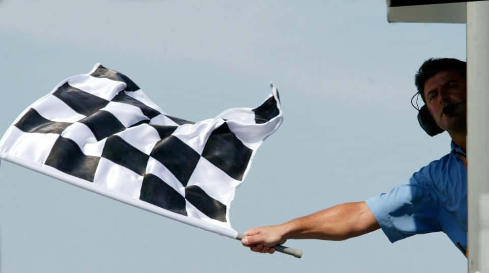 Chequered Flag 桌布 壁紙 — 賽事工作人員在晴朗的天空下揮動格仔旗，進行賽車活動。