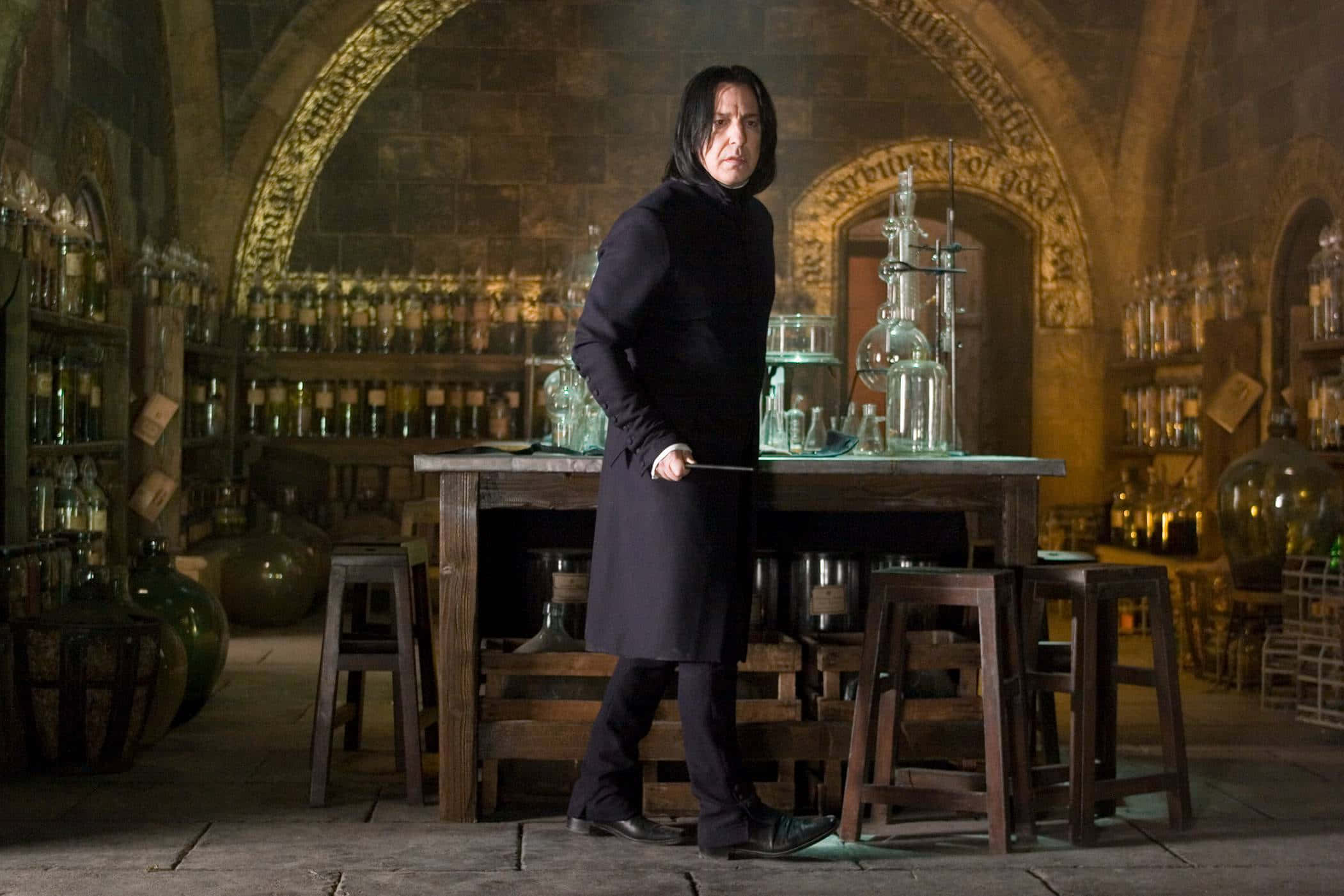 The Hogwarts Potions Class 桌布 壁紙 — 賽佛勒斯·石內卜站在燈光昏暗的魔藥學教室，周圍是裝滿玻璃瓶的架子和冒泡的坩堝。