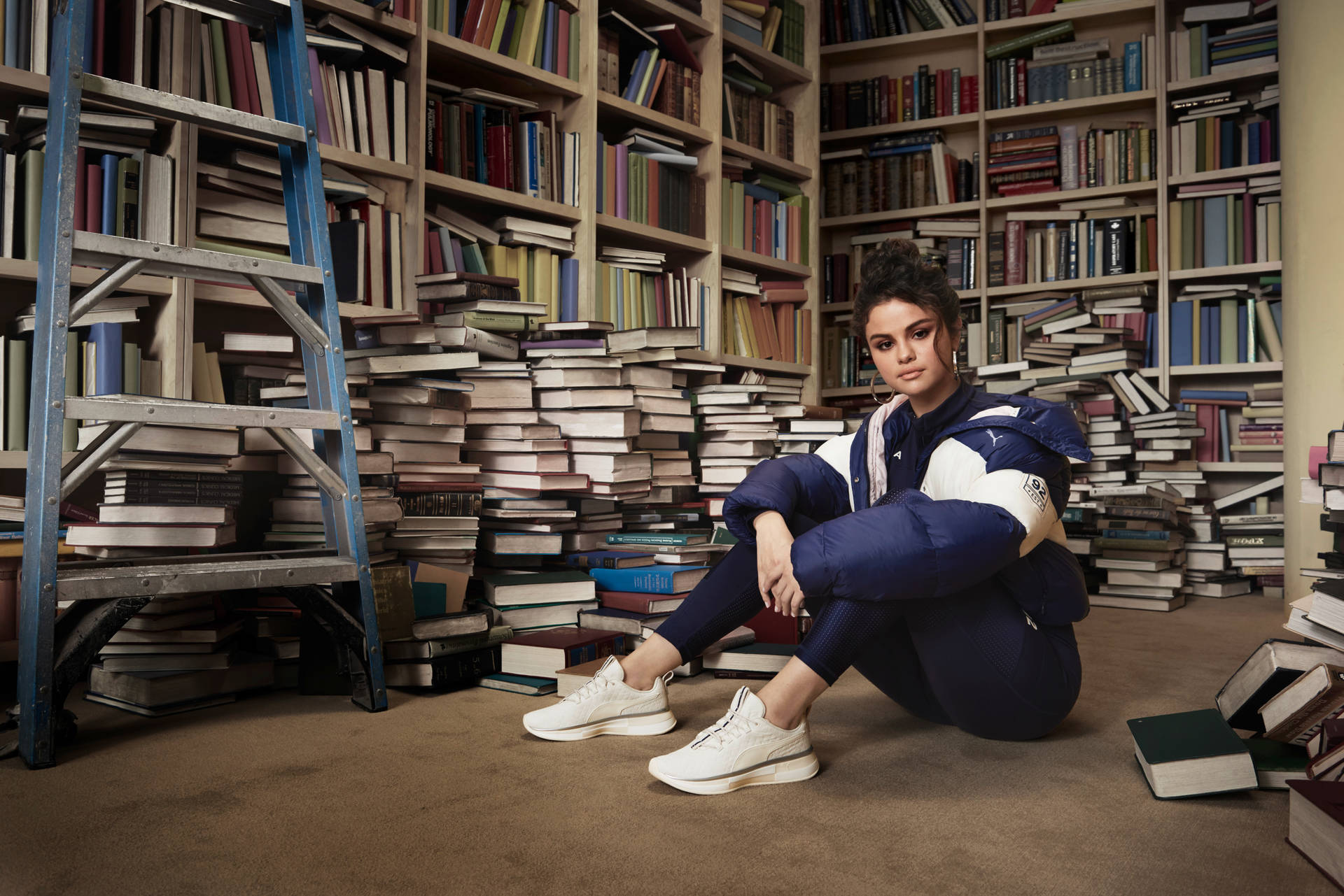 Selena Gomez 坐在圖書館的書堆中，旁邊有一把藍色梯子。