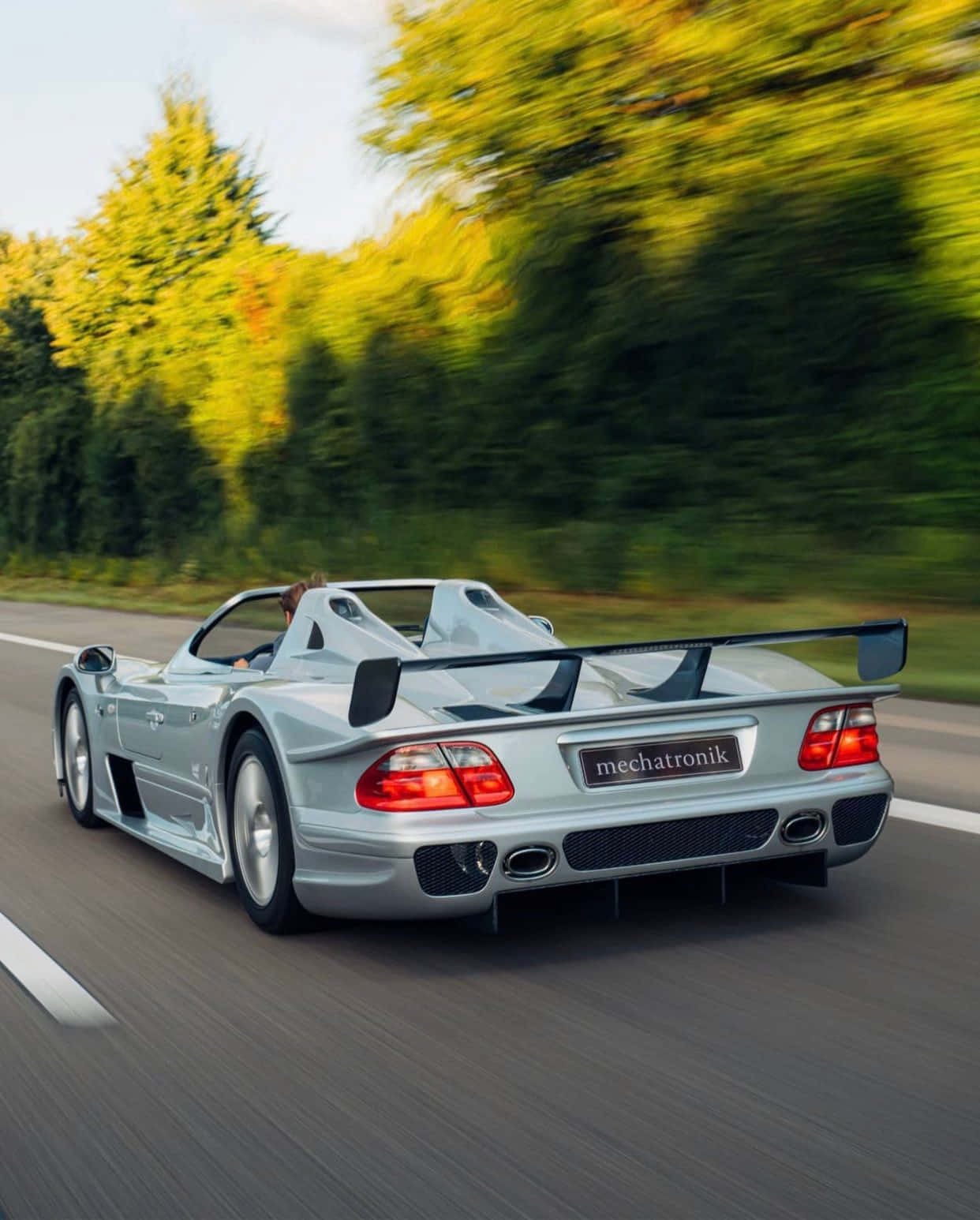 賽車綠樹安卓AMG GT-R背景 壁紙 — 一輛銀色 Mercedes-Benz CLK GTR Mechatronik 在樹林環繞的道路上疾馳，動態模糊強調了速度。