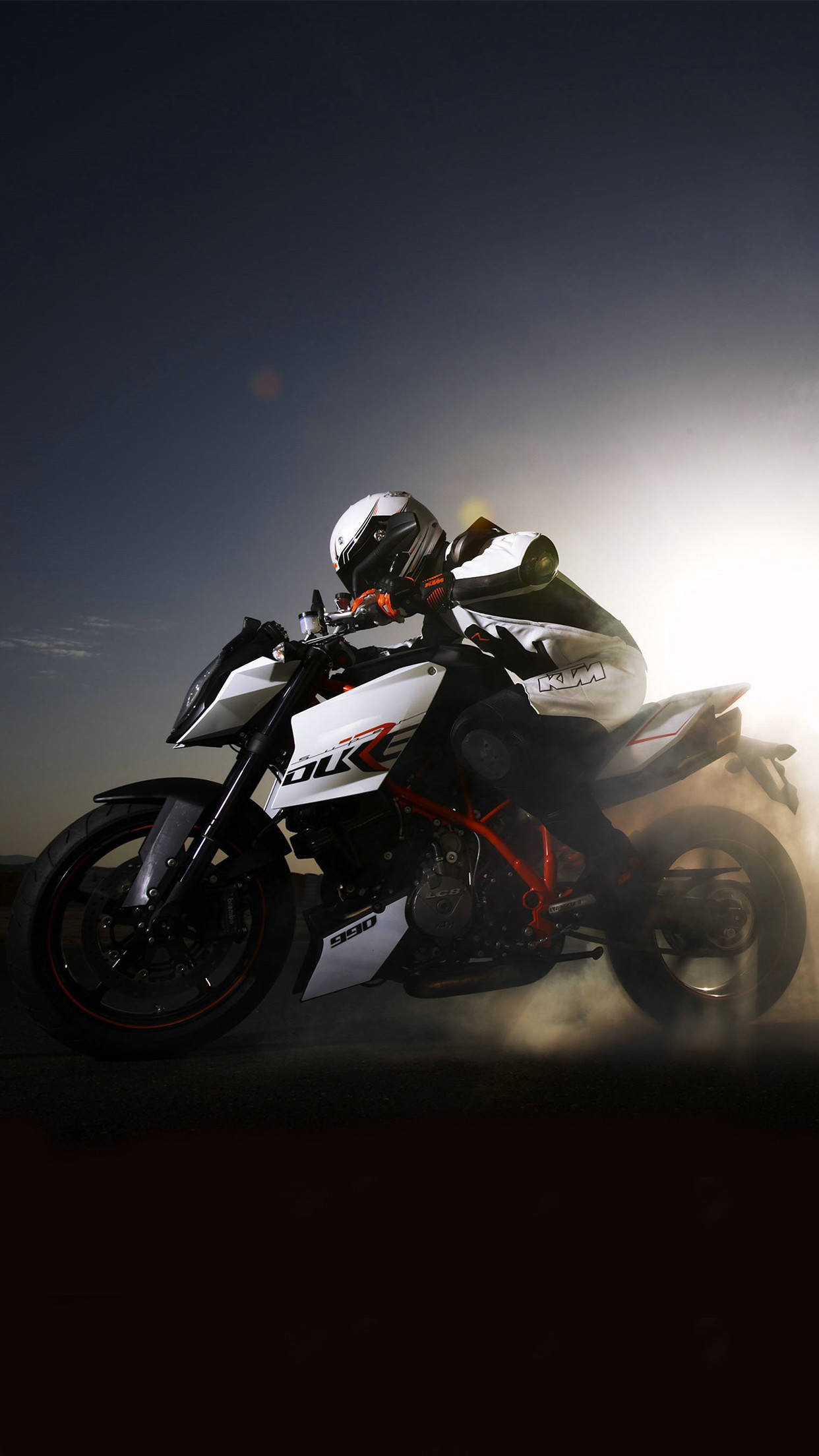 賽道上的KTM 990 Duke賽車 壁紙 — 一名騎手騎著白色和紅色的KTM Duke電單車，在燦爛的夕陽天空下揚起灰塵，傾身入彎。