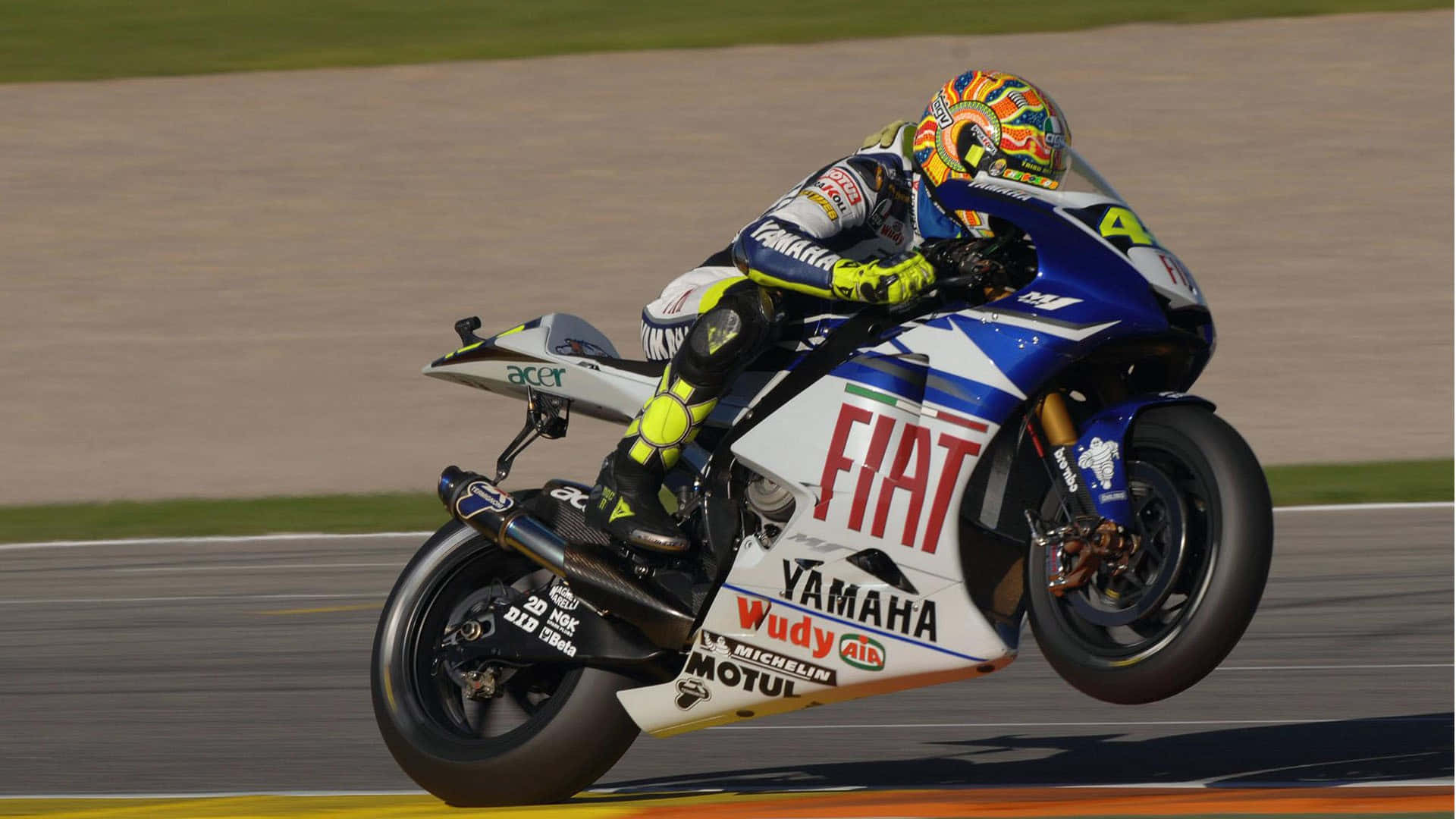 賽道之王：VR46馳騁賽道 壁紙 — 一位電單車手在賽道上騎著藍白相間的Yamaha賽車，帶有Fiat品牌標誌，傾斜入彎。