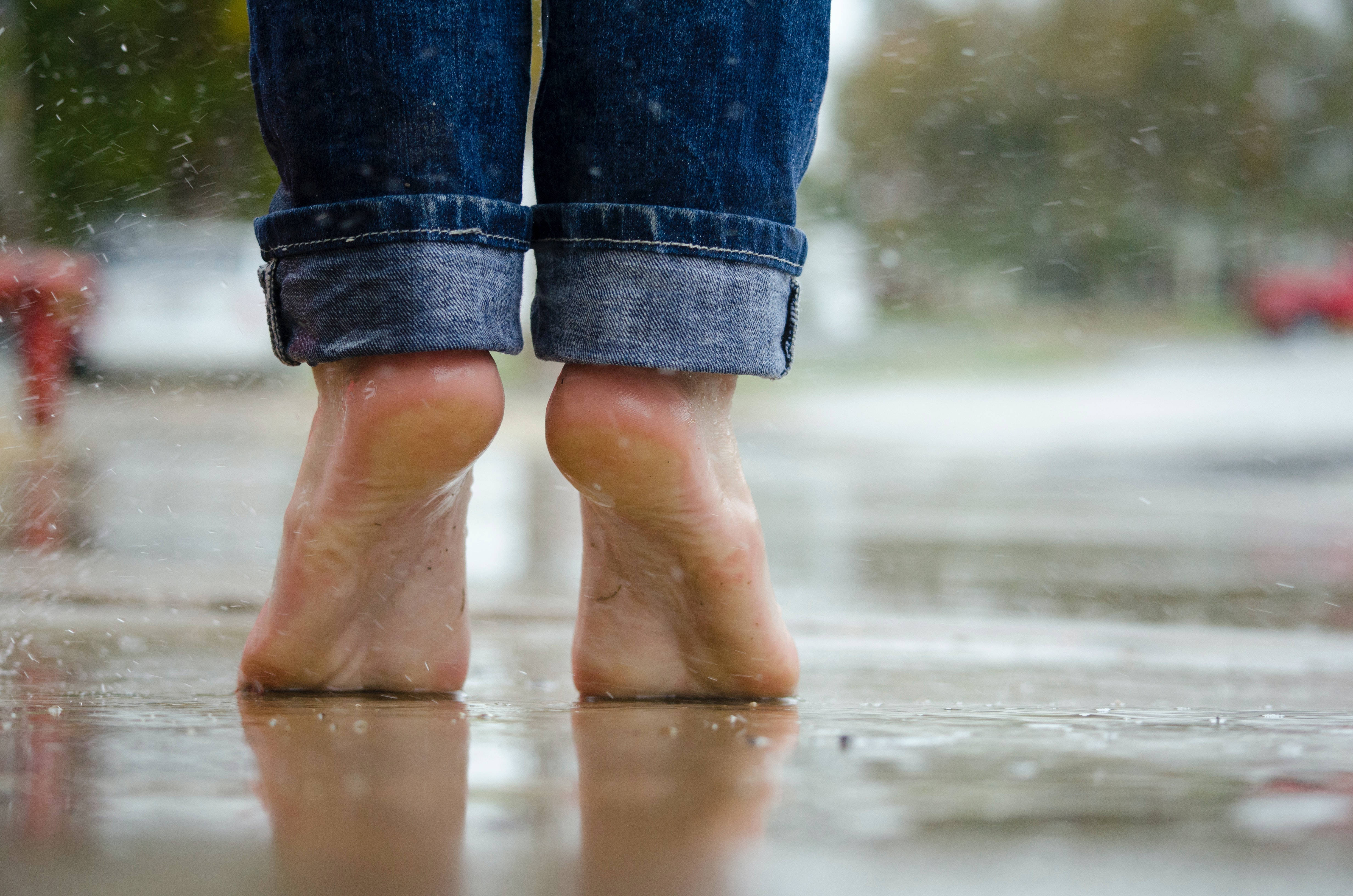 feet 桌布 壁紙 — 赤腳站在濕漉漉的人行道上，雨滴落在捲起的牛仔褲周圍。