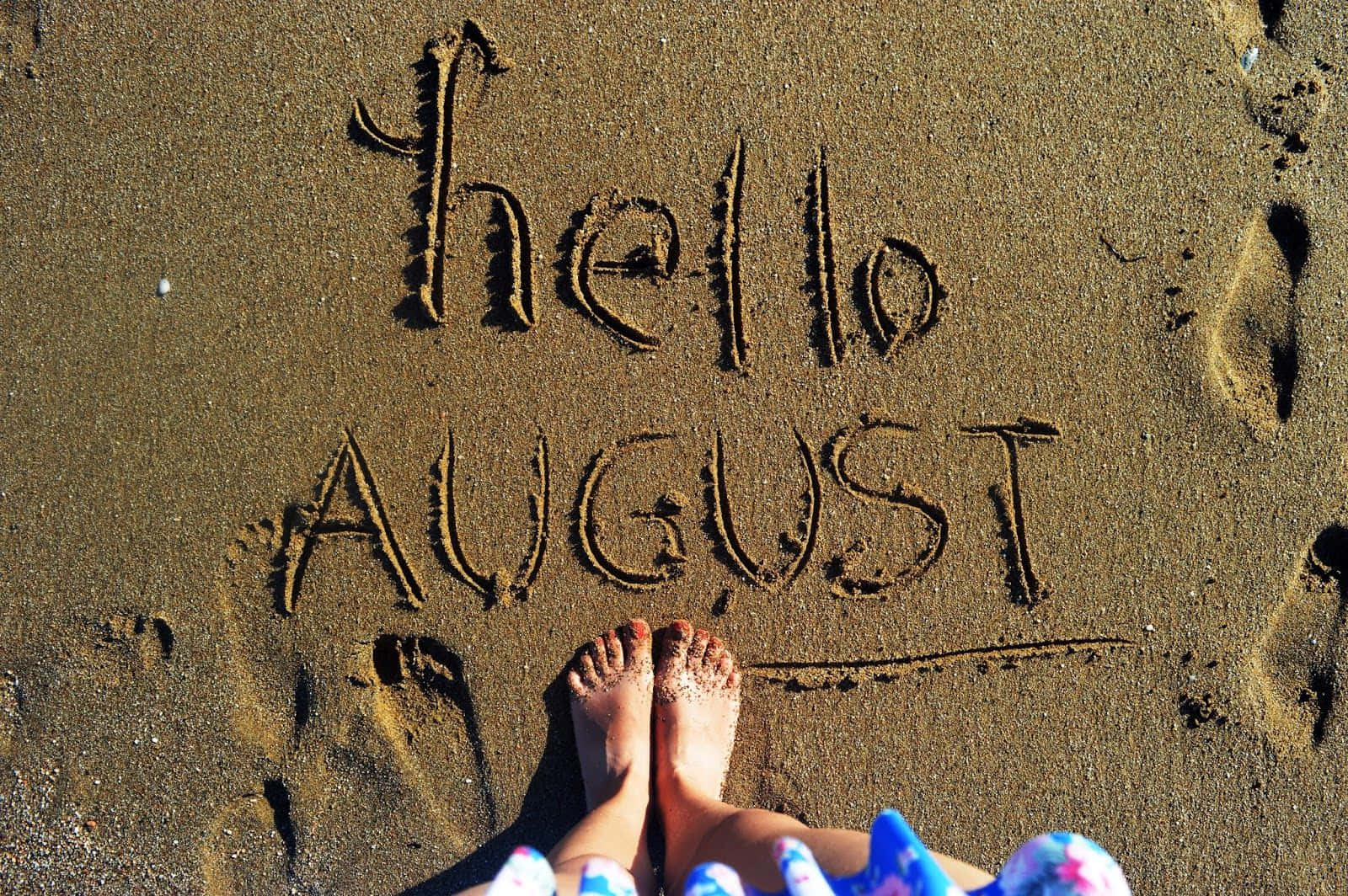 August 桌布 壁紙 — 赤腳站在陽光照耀的沙灘上，旁邊用草書和印刷體寫著「hello AUGUST」。