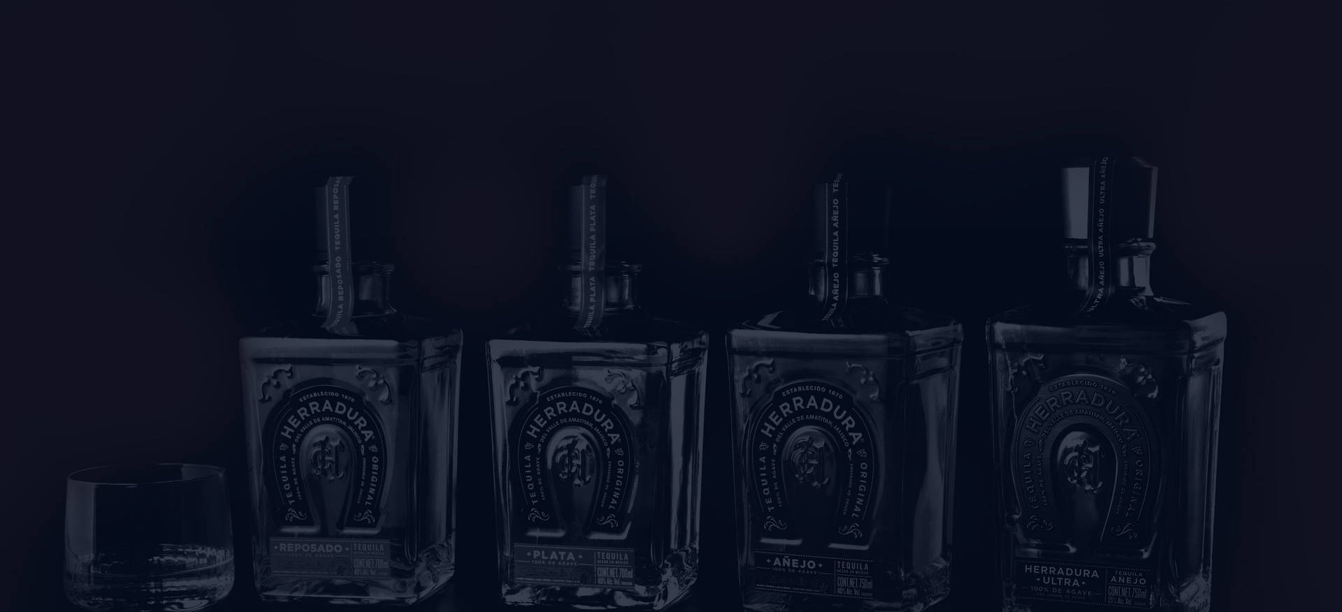 四瓶 Herradura 龍舌蘭酒和一個玻璃杯在黑暗的表面上。