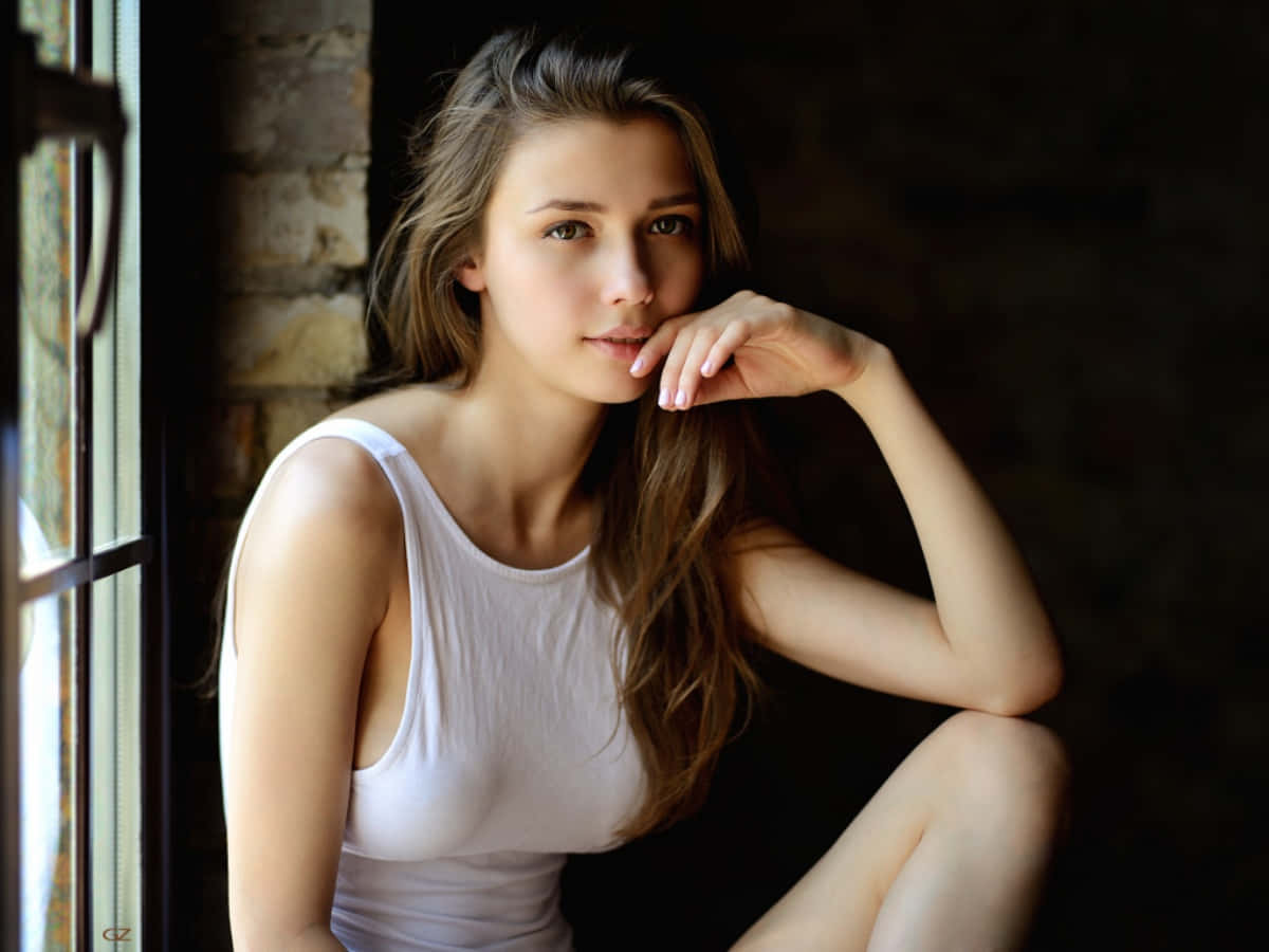 身穿白色背心的年輕女性坐在磚牆背景的窗邊。