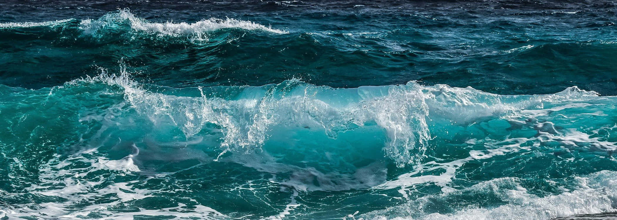 超寬海景美學圖 壁紙 — 強勁的綠松色海浪在明亮的陽光下撞擊深藍色的大海，激起白色泡沫。