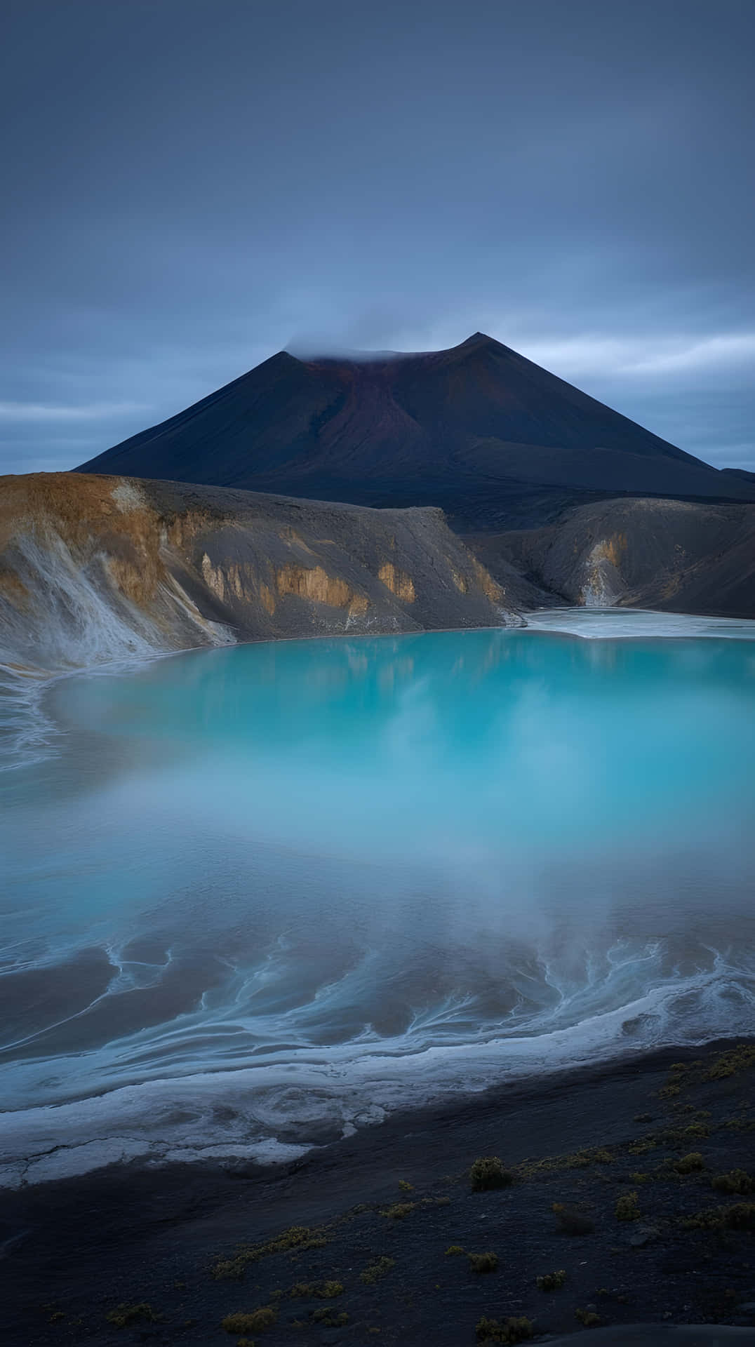 綠松色火山湖在暮色天空下映照黑暗山脈