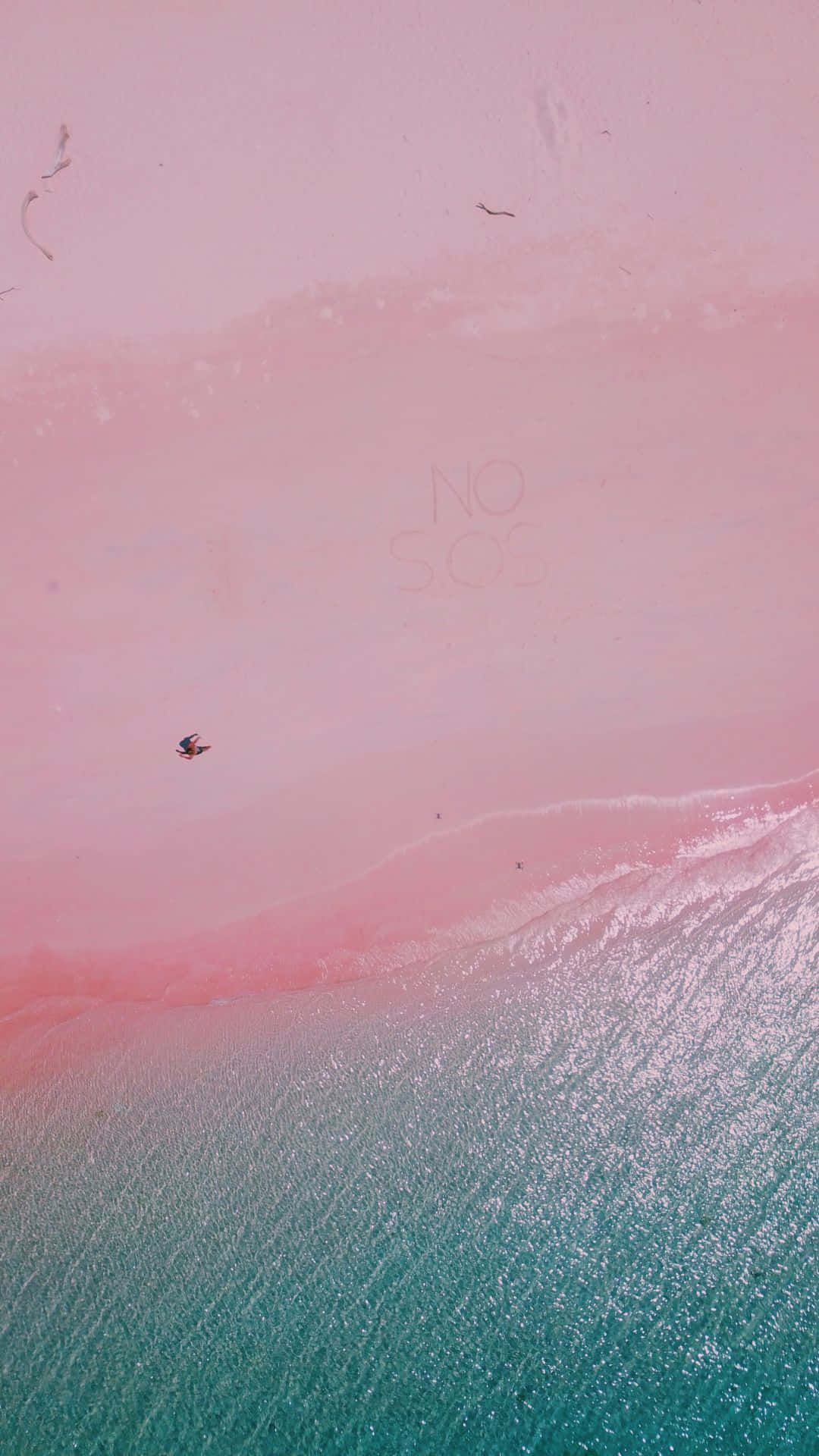 Pink Beach 桌布 壁紙 — 超現實粉紅色海灘與碧綠海水交匯的航拍圖，沙灘上隱約刻有「NO SOS」字樣，附近有一個孤獨的身影。