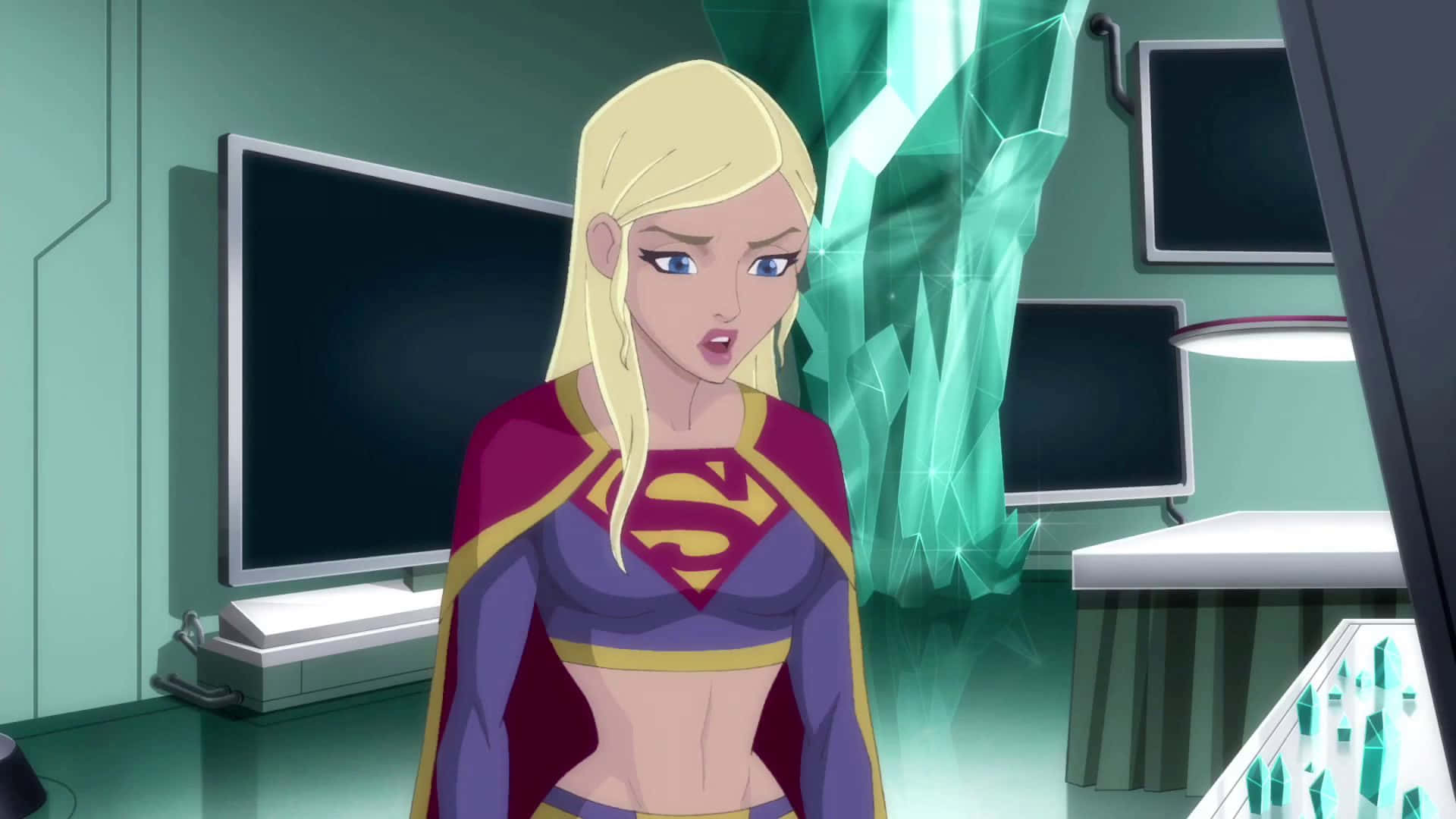 Superman Unbound 桌布 壁紙 — 超級女孩站在一個高科技實驗室裡，身後有發光的綠色水晶和顯示器。