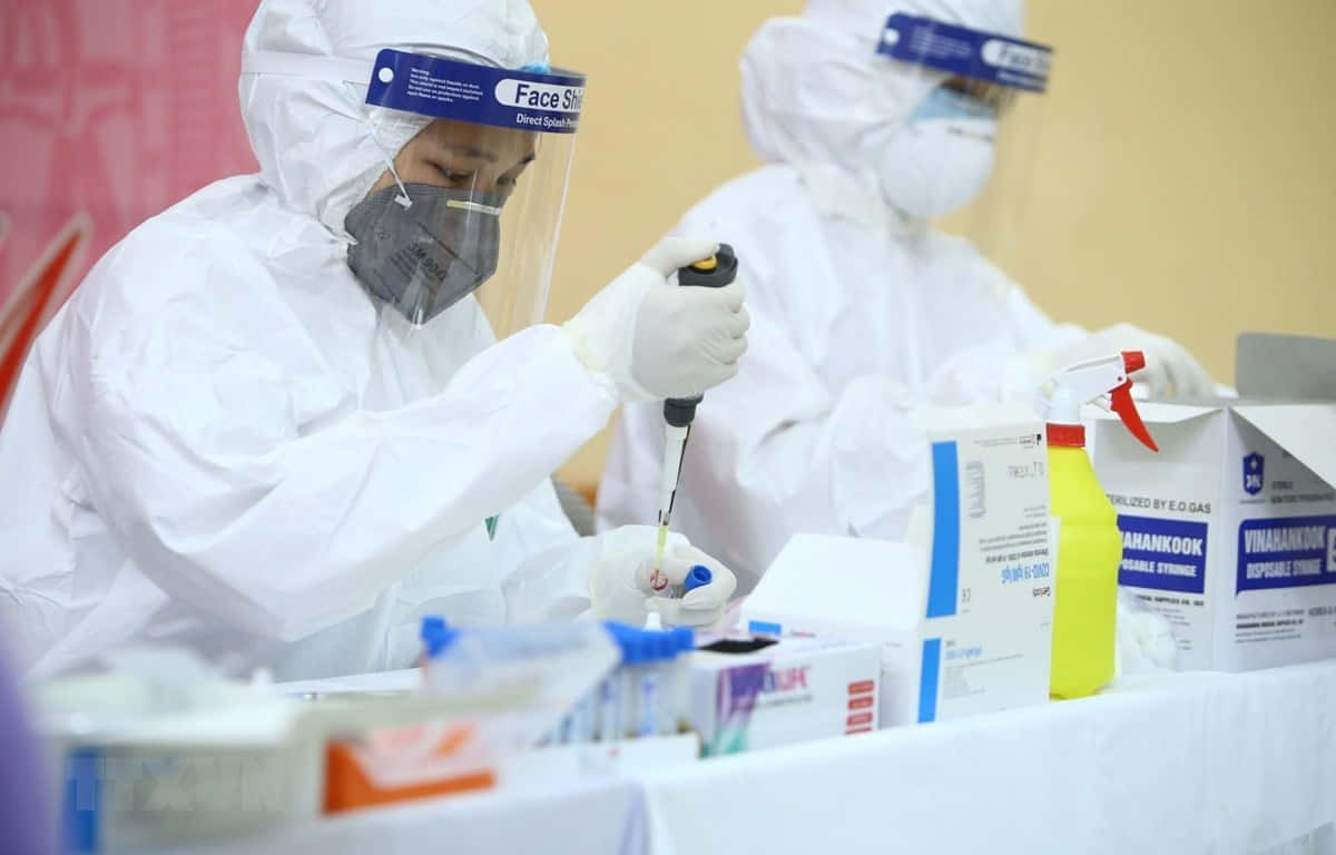 超級英雄笑容的醫生 壁紙 — 醫護人員穿著全套防護裝備，在健康篩查操作期間於實驗室站小心處理試管。