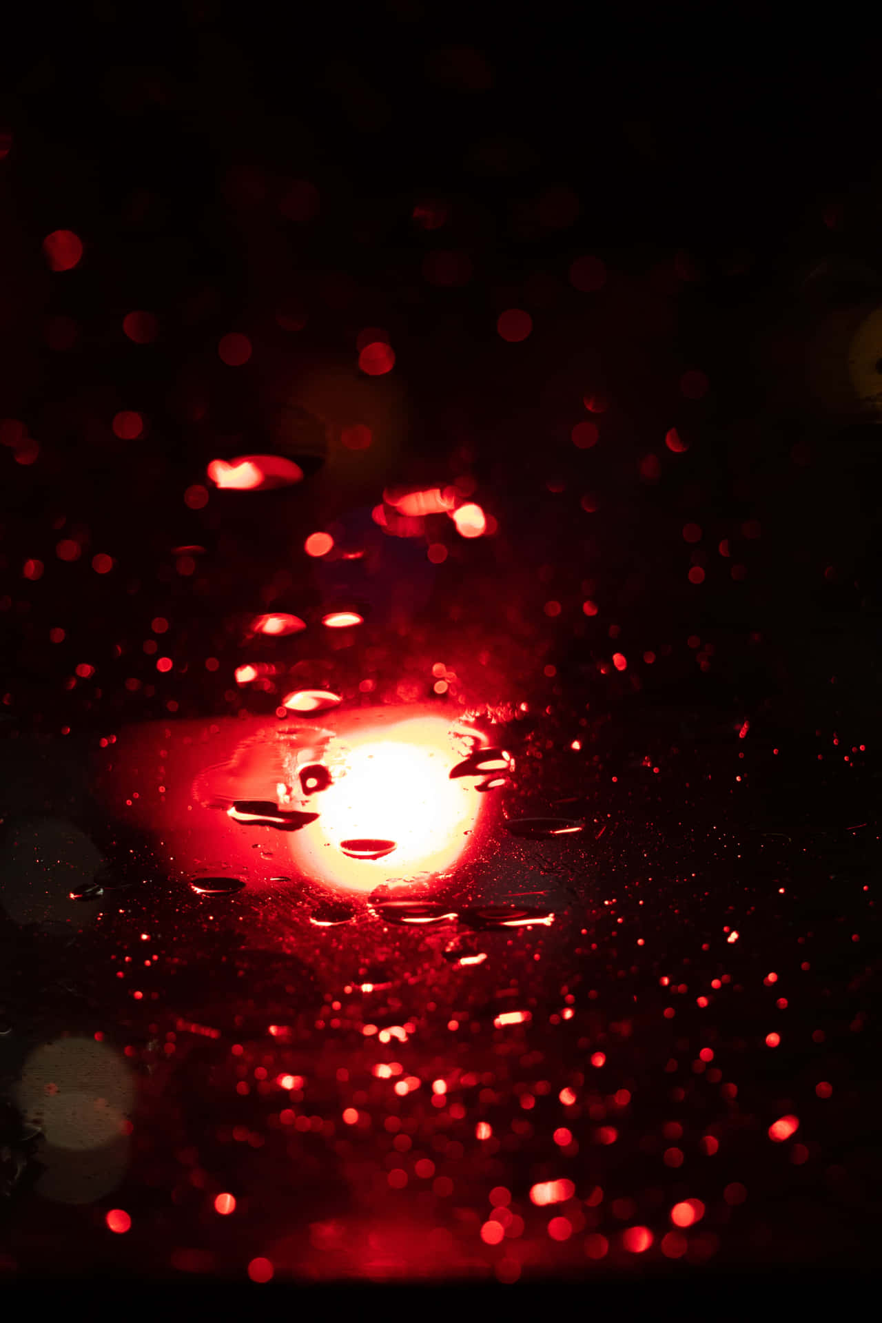 玻璃上的雨滴在黑暗中反射出微弱的紅光。