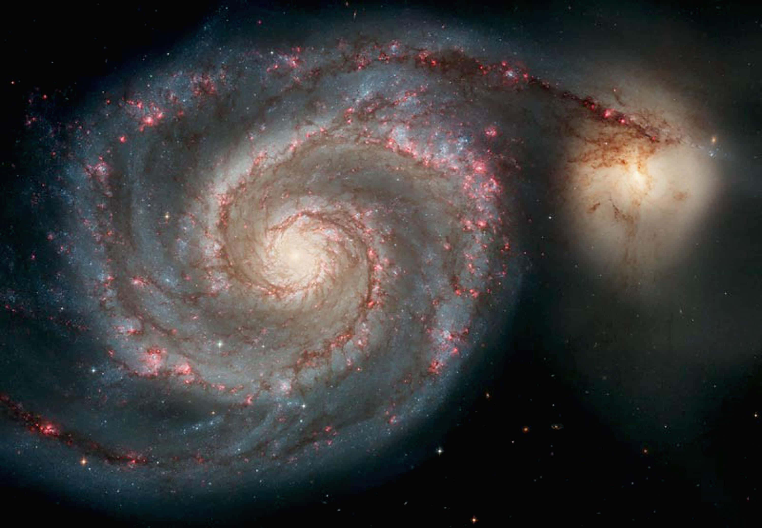 「超越我們極限的視野，透過這張令人驚嘆的NASA星系圖片！」 壁紙 — 一個宏偉的螺旋星系在繁星點點的宇宙虛空中旋轉，伴隨著發光的紅色恆星和藍色塵埃帶。