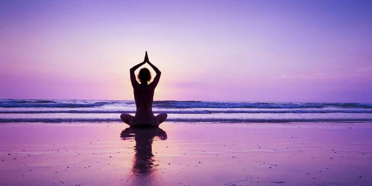 一個人在日落時分在海灘上冥想，紫色天空和海洋波浪。