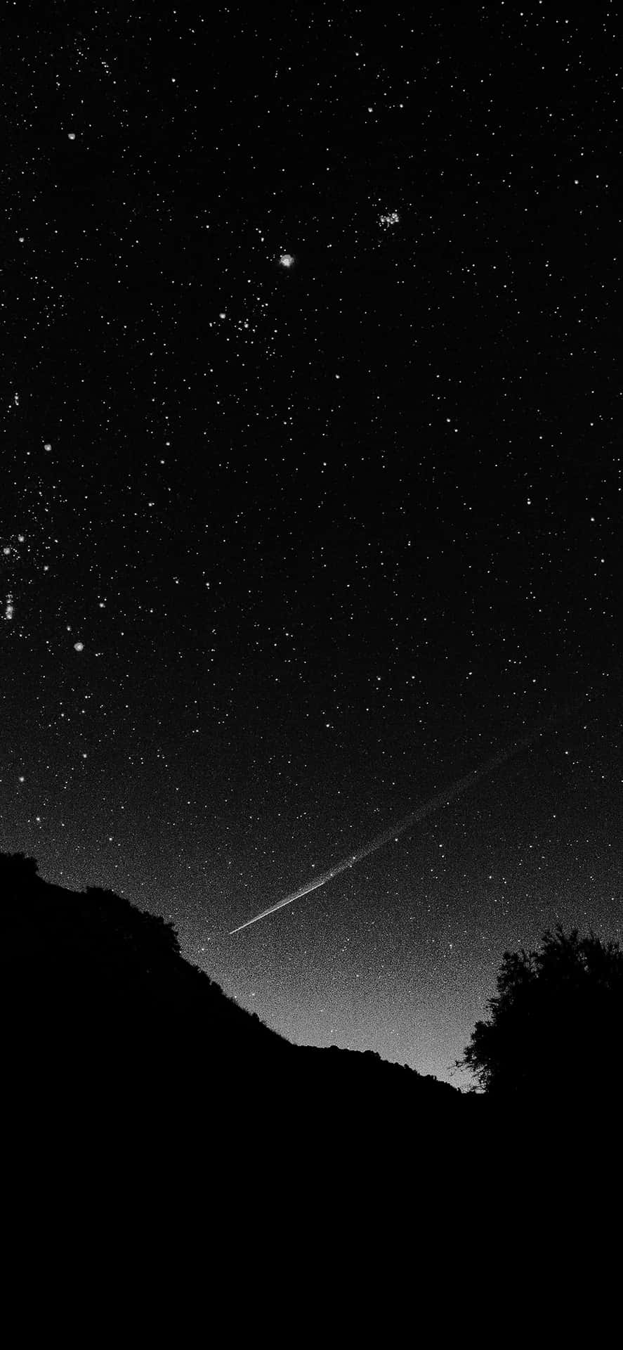 一顆流星劃過黑暗山丘和樹木上方的星空夜空。