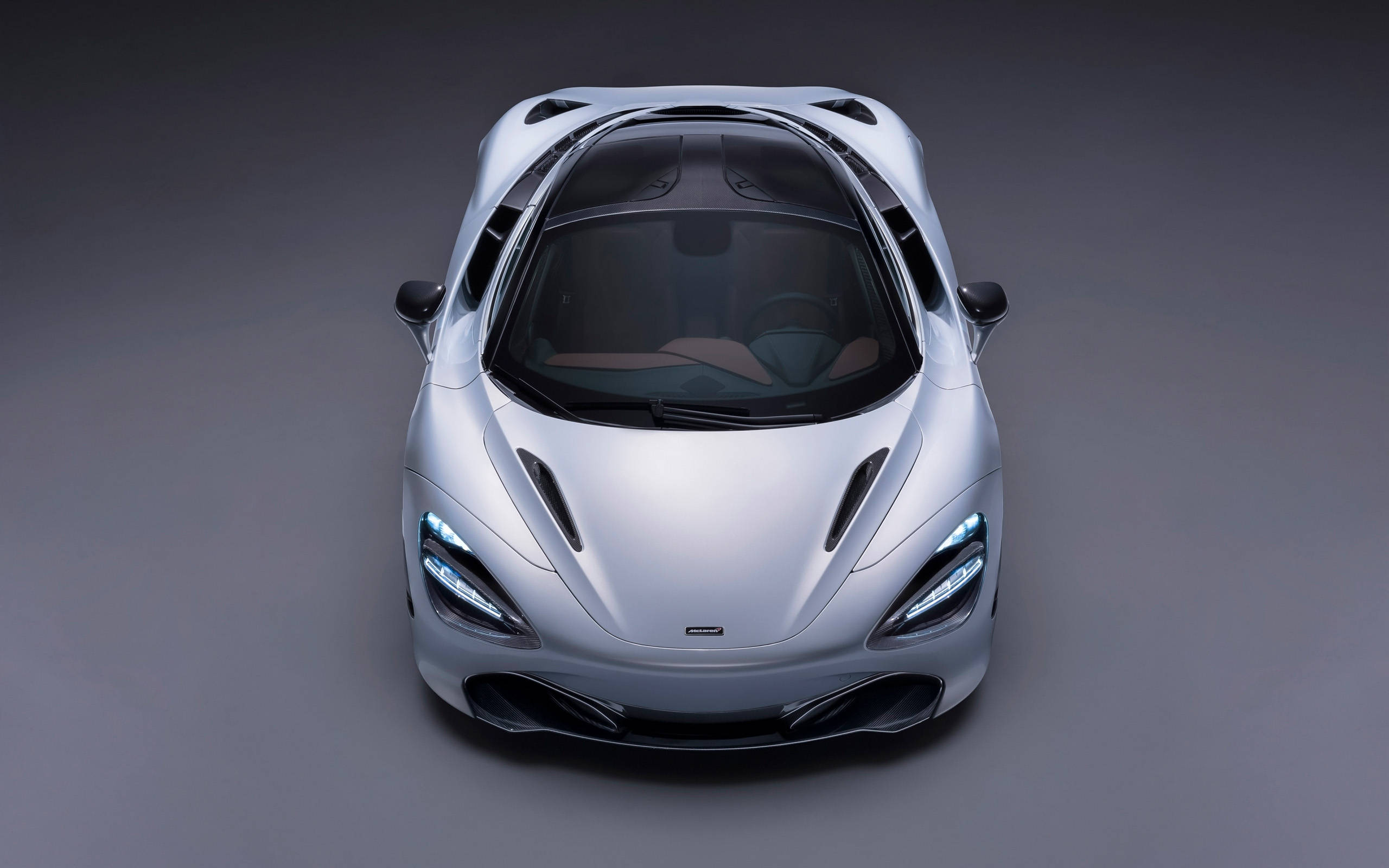 超跑麥拉倫720S 4K 壁紙 — 一輛時尚的銀色跑車從上方觀看，車頭燈發光，背景為深灰色工作室。
