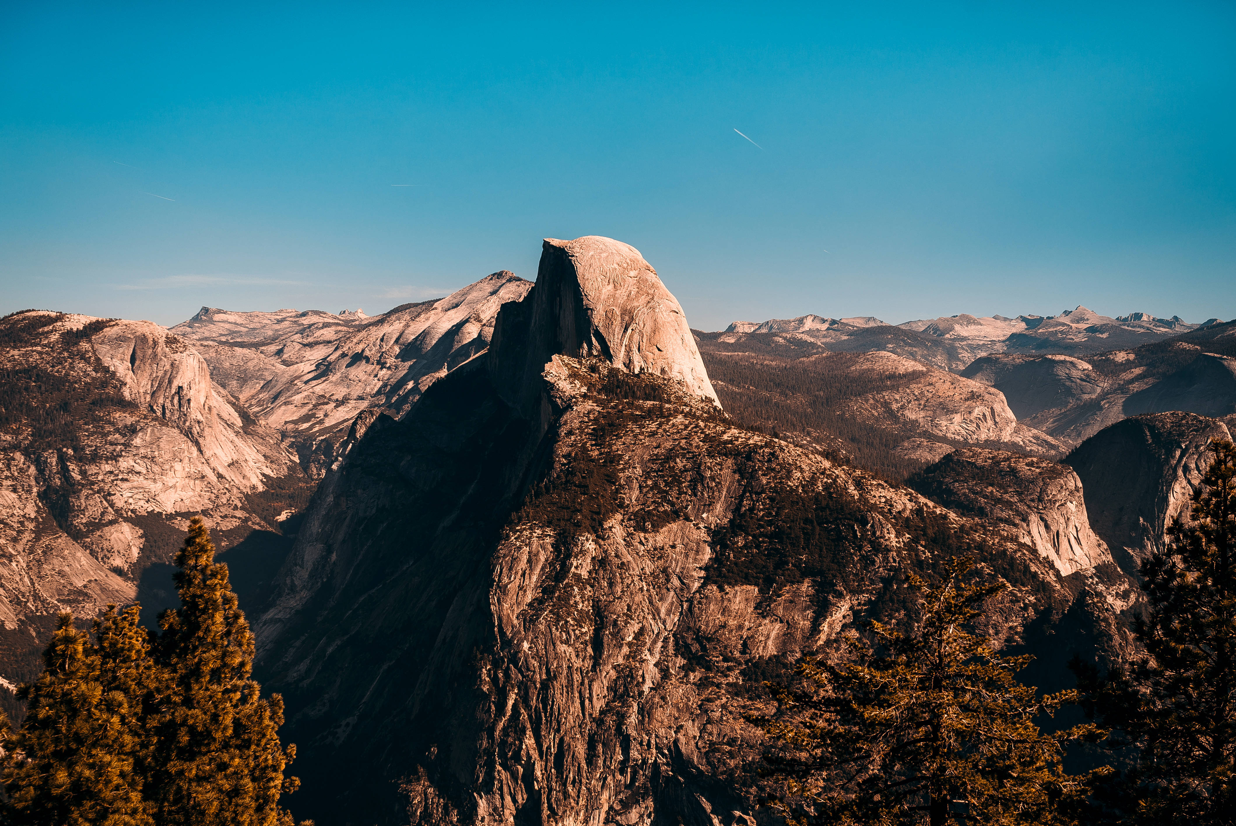 超酷的優勝美地半圓頂 壁紙 — Half Dome 雄偉地聳立在清澈的藍天下，金色的陽光照射在其花崗岩表面和周圍的山脈上。