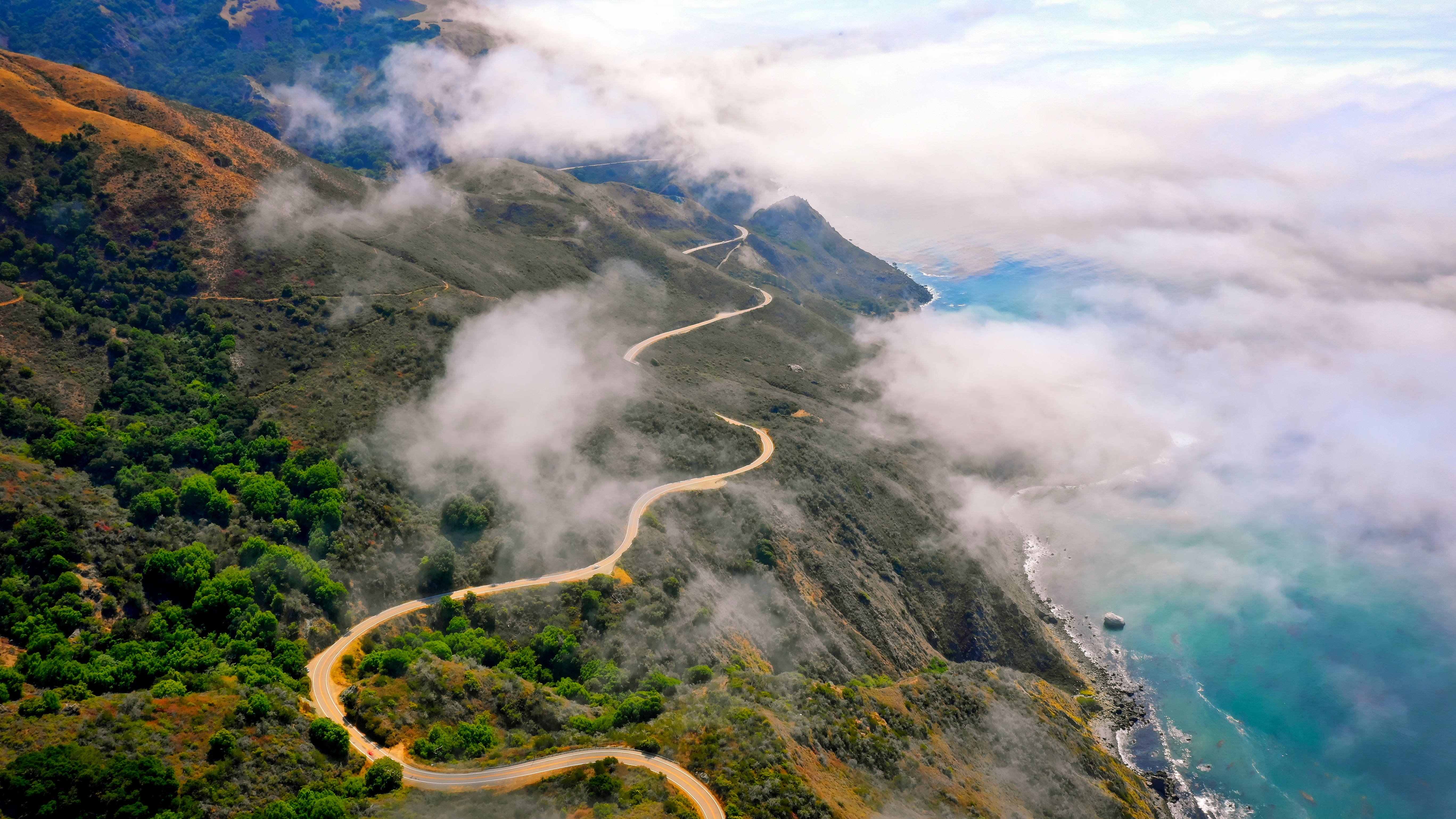 超酷的加州公路 壁紙 — 一條蜿蜒的海岸公路穿過煙霧繚繞的山脈，俯瞰著碧綠色的海水。