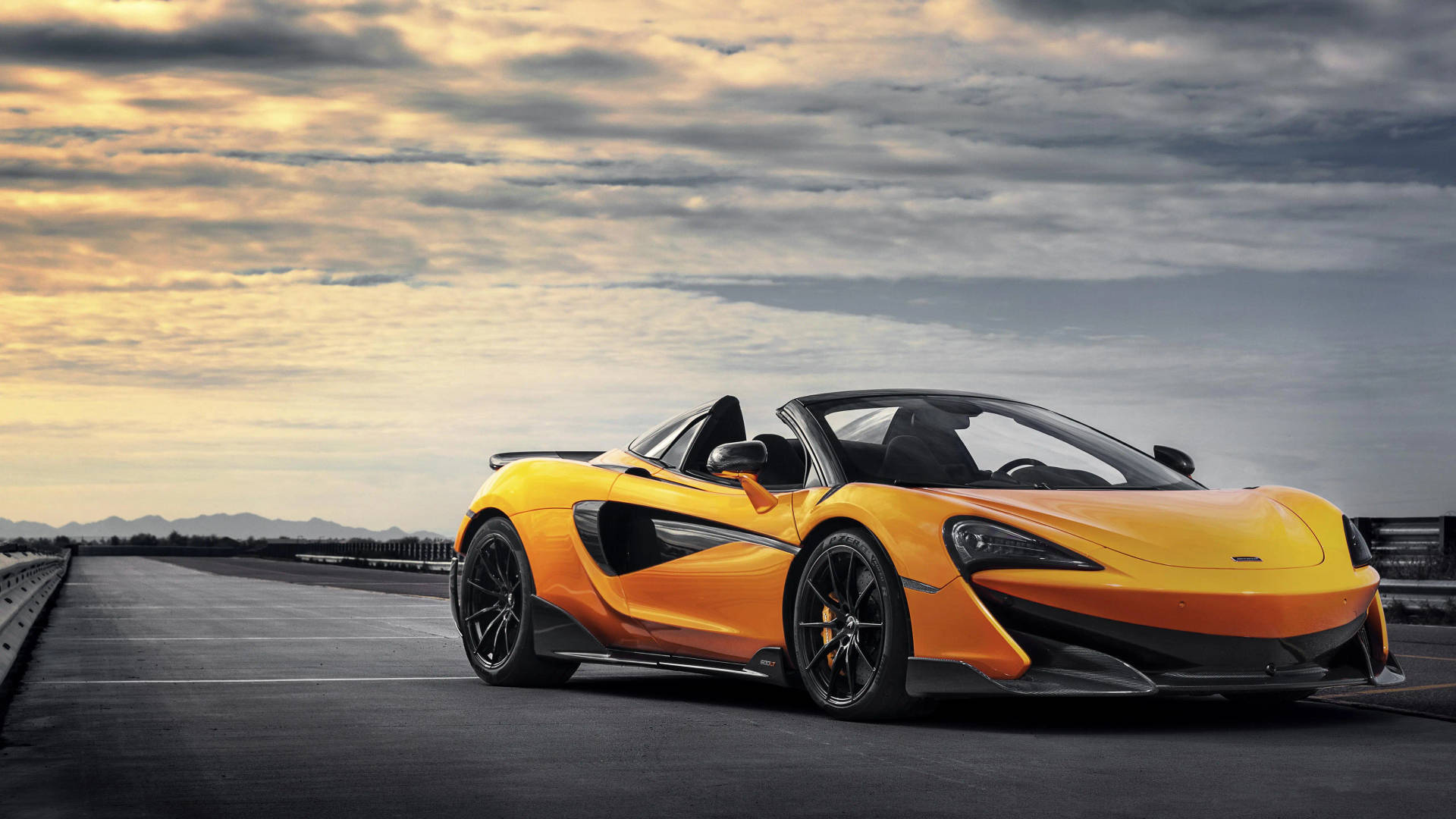 日落時分賽道上的橙色McLaren跑車與戲劇性的雲層。
