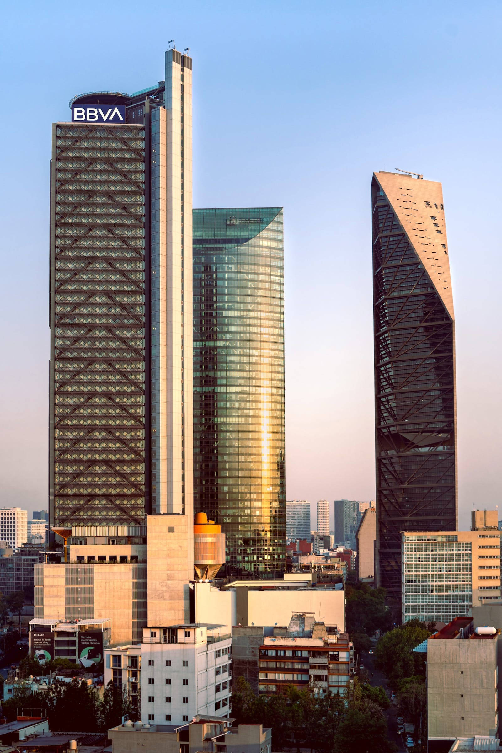 超高解析度摩天大樓群 壁紙 — 現代摩天大樓帶有BBVA標誌，在清澈的藍天下聳立，金色陽光在玻璃外牆上閃爍。
