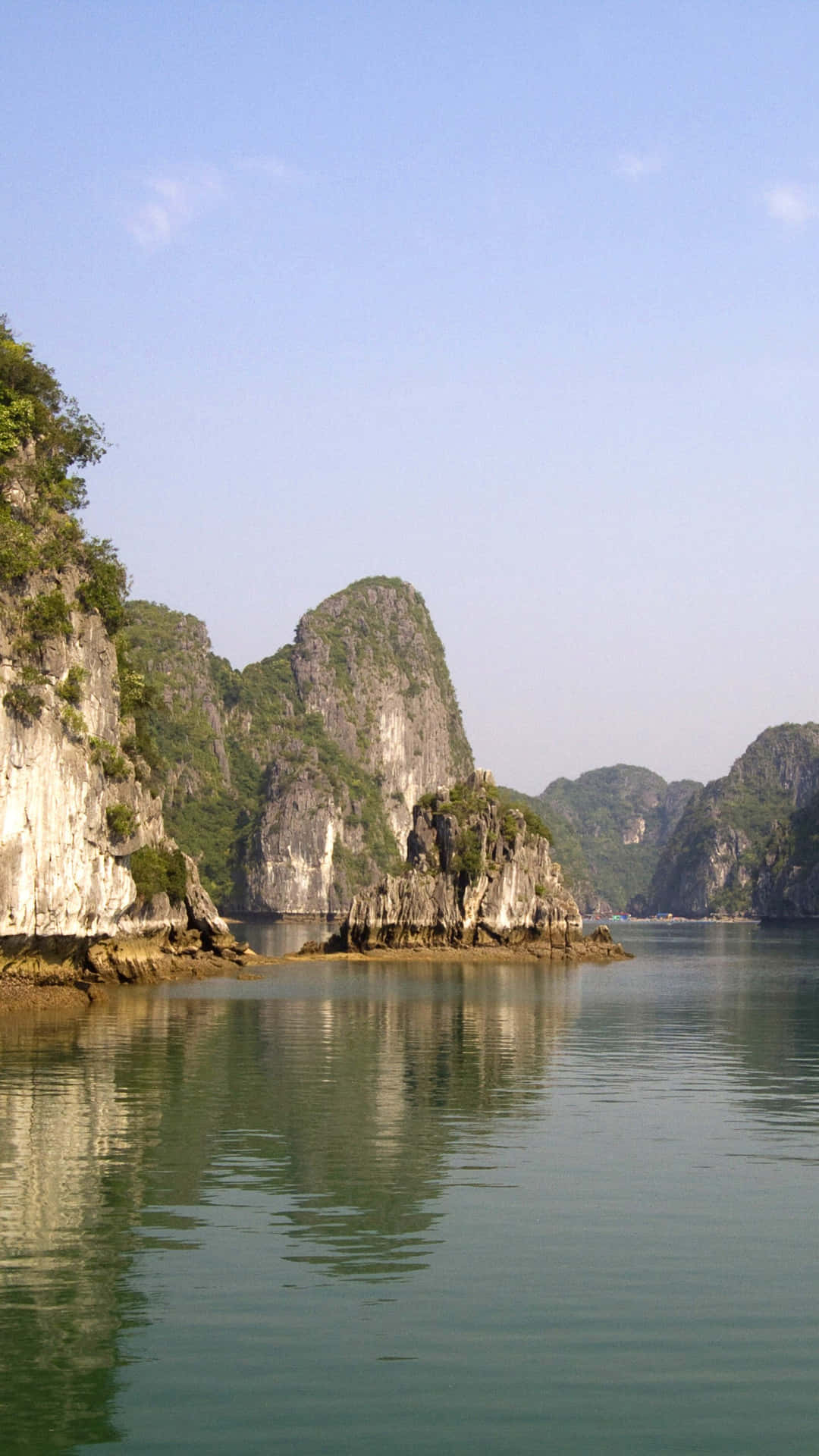 寧靜的海灣，高聳的石灰岩喀斯特地貌倒映在平靜的碧綠海水中，天空晴朗湛藍。