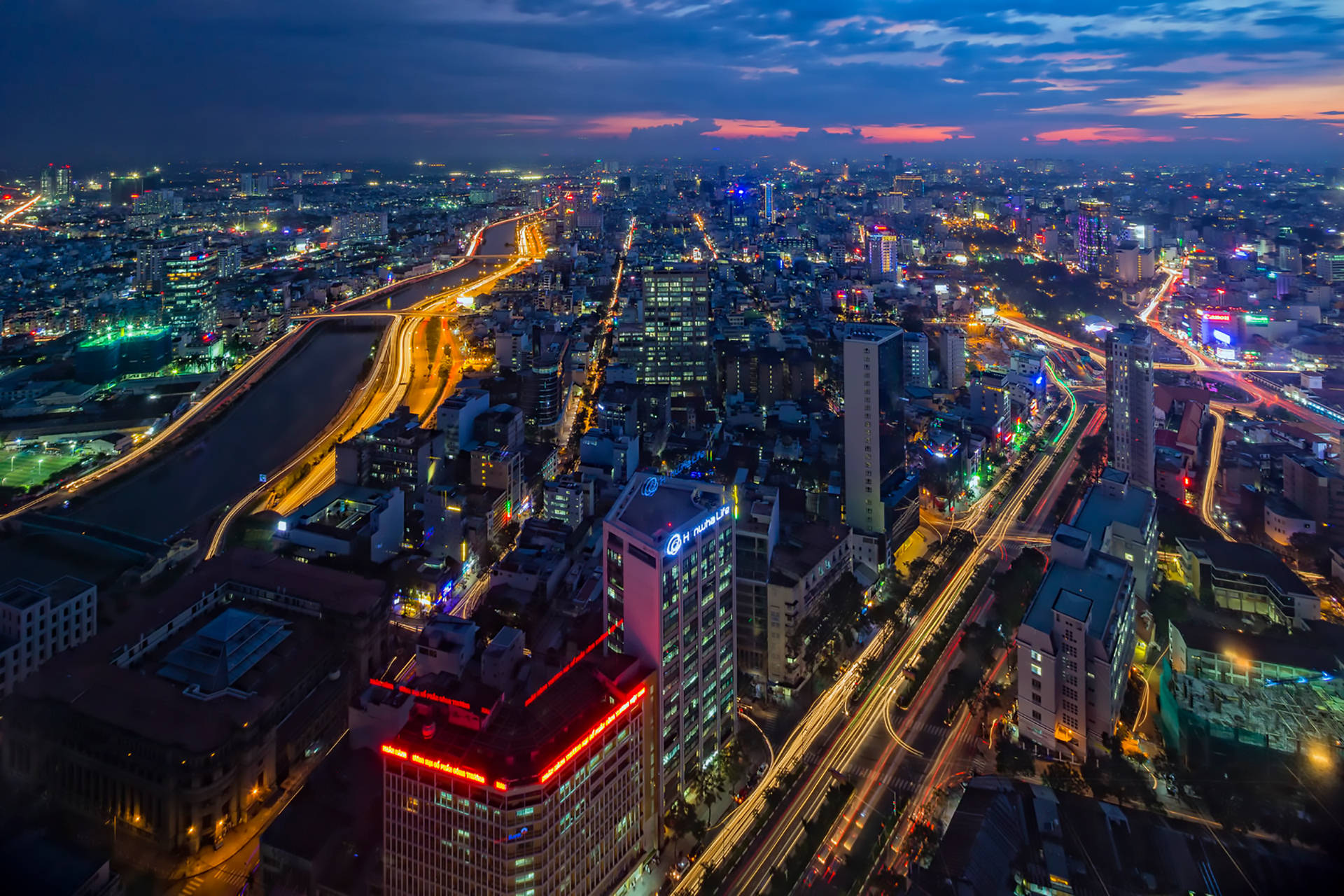 越南夜間城市燈光 壁紙 — 黃昏時分繁忙城市的鳥瞰圖，霓虹燈閃爍，車流光軌照亮城市擴展區。