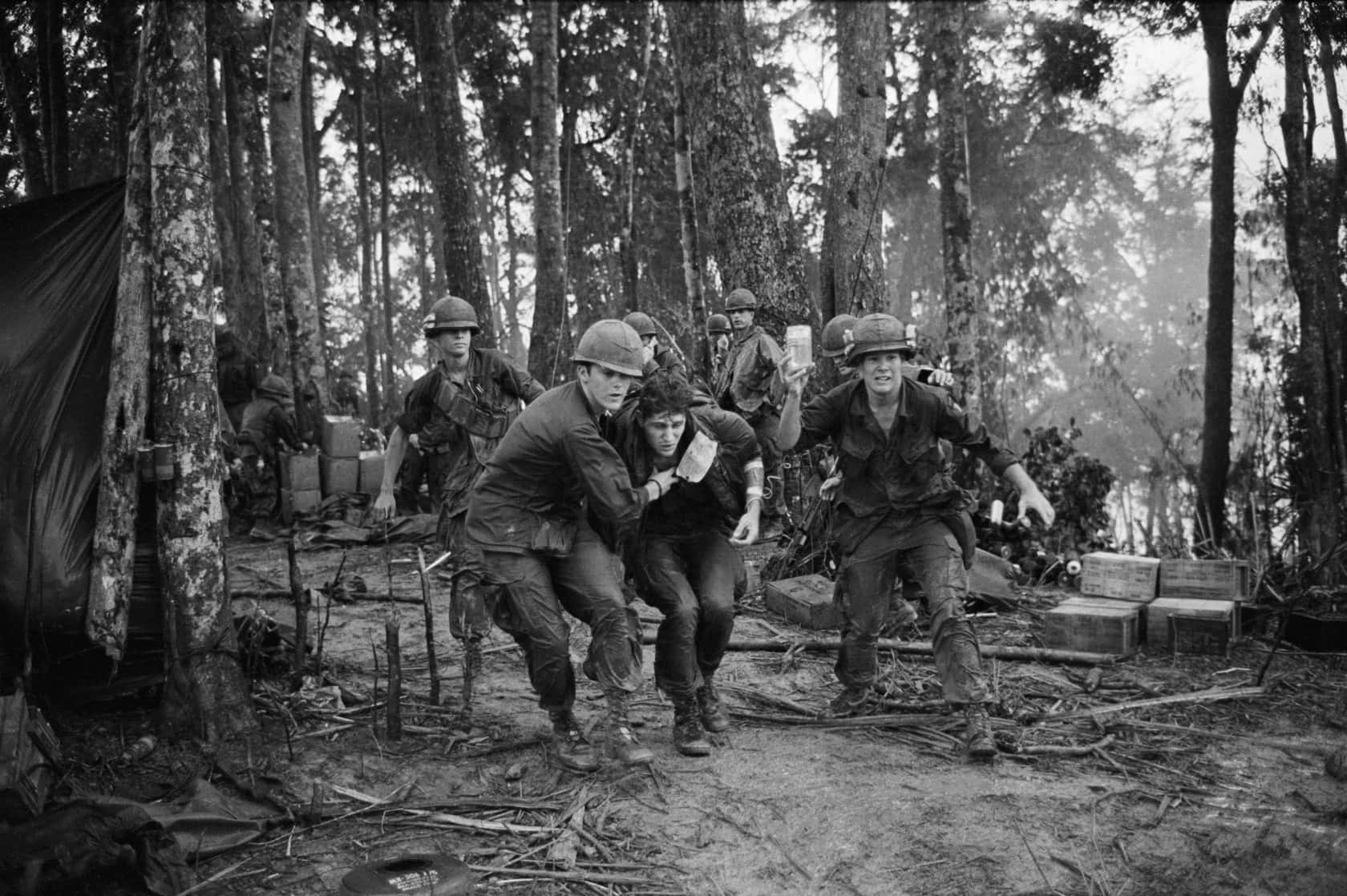 士兵抬著一名受傷的戰友穿過泥濘的叢林營地。