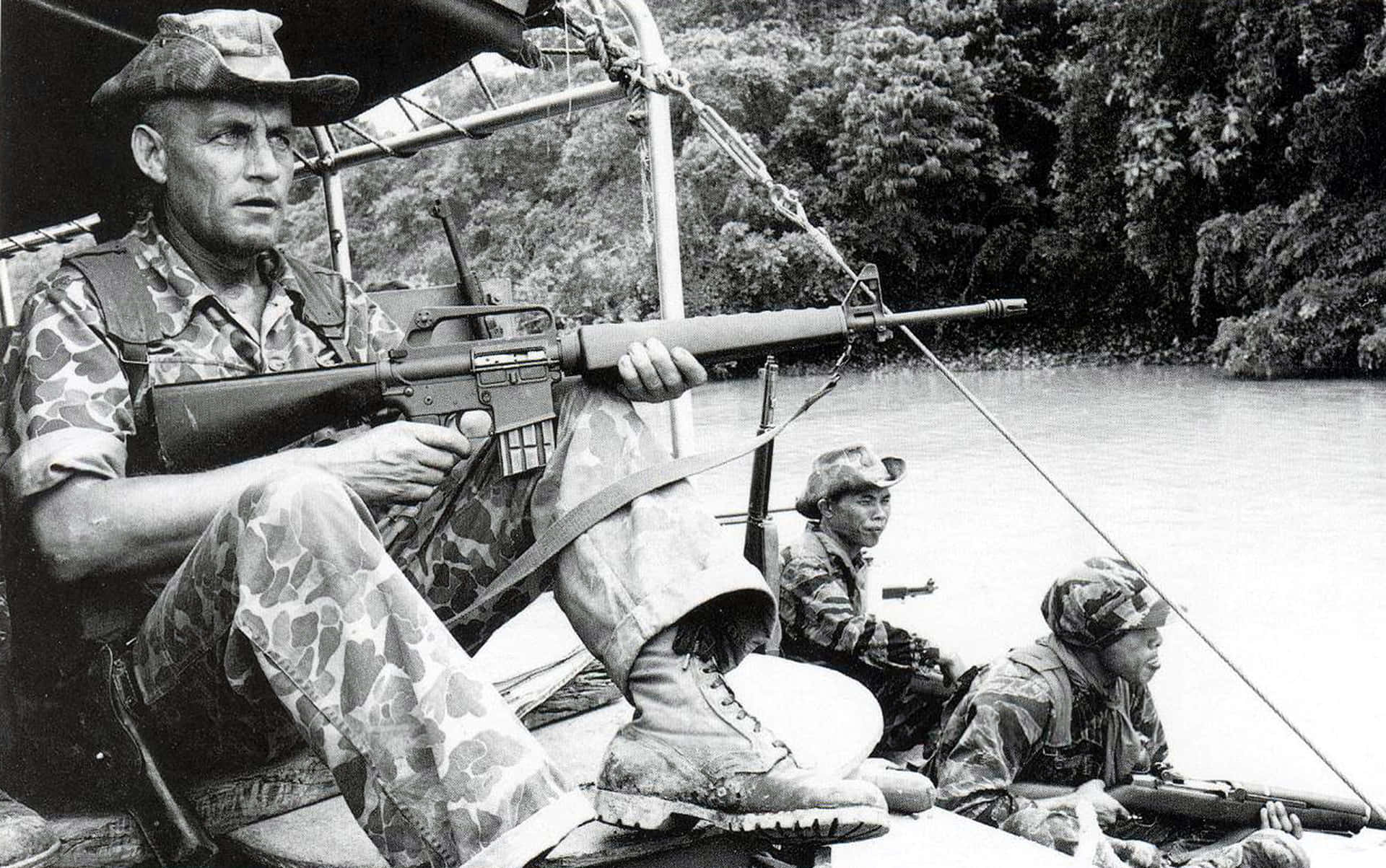 三名身穿迷彩軍服的武裝士兵在叢林環境中的河船上。