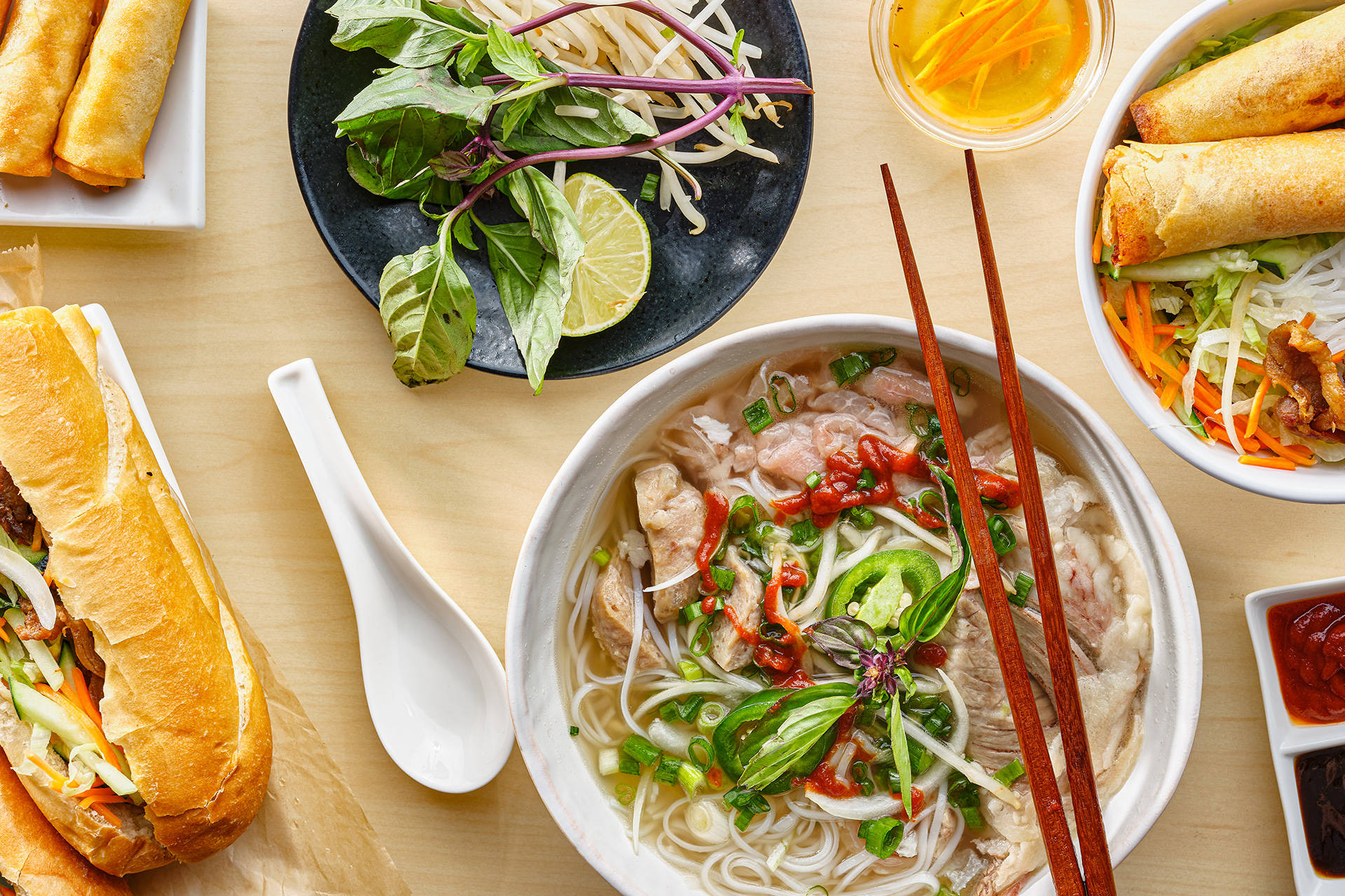 越南菜餚，河粉、春卷和越南法包在木桌上。