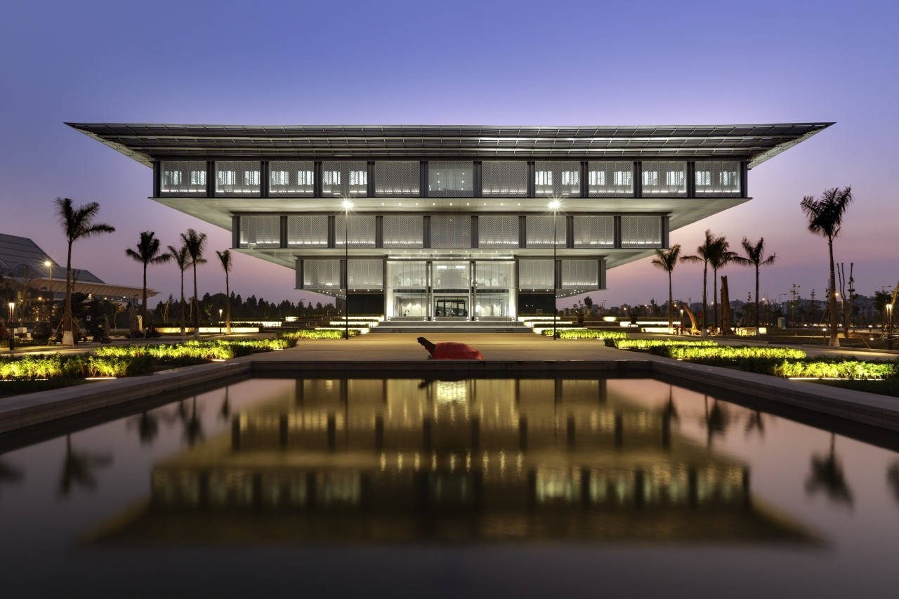 越南河內博物館壯麗景觀 壁紙 — 一座現代玻璃建築，帶有浮動屋頂，在黃昏時分倒映在寧靜的水景中，周圍環繞著棕櫚樹。