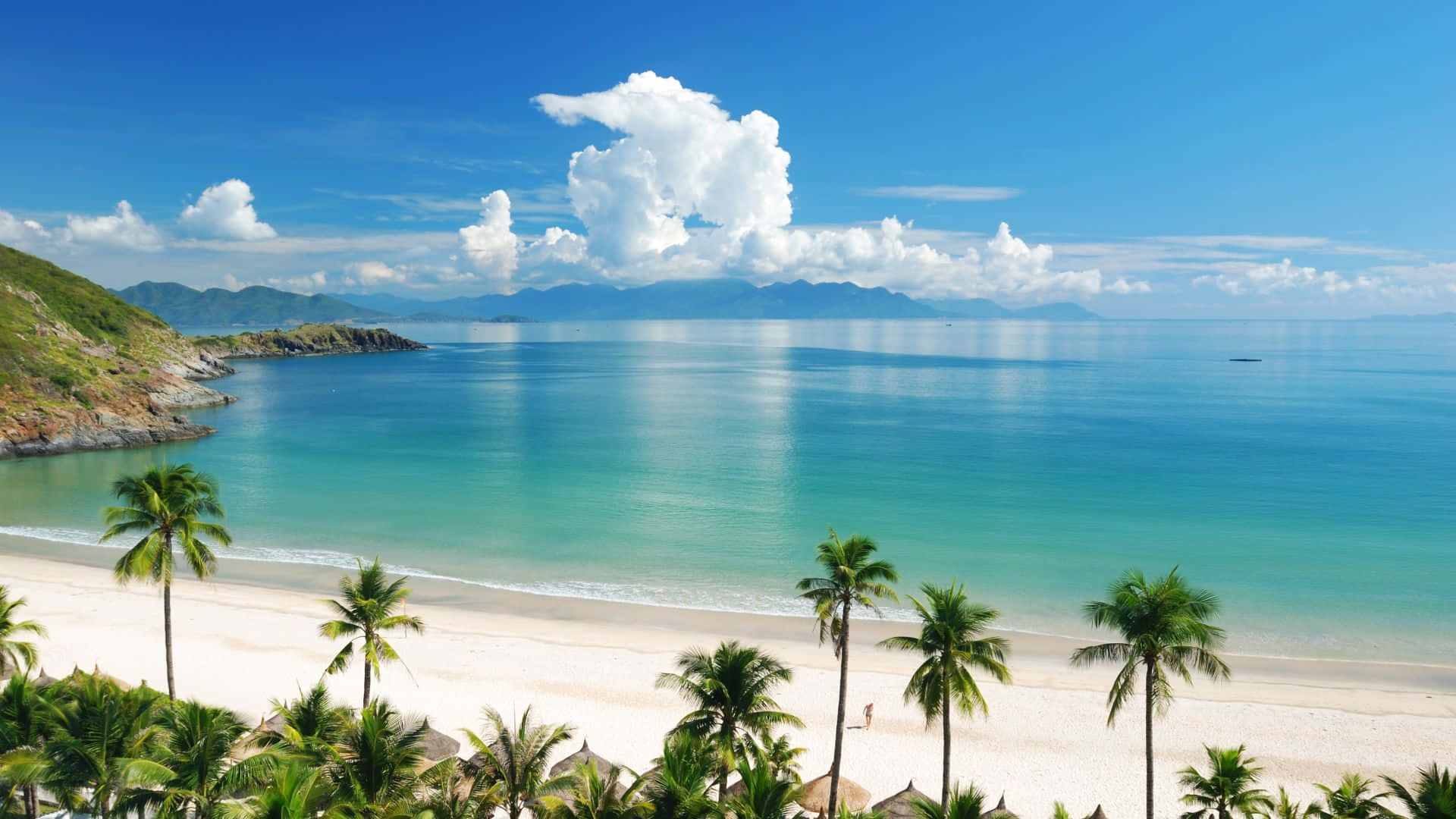 越南美溪海灘主題背景 壁紙 — 一個令人驚嘆的熱帶海灘，擁有碧綠的海水、白色的沙灘和棕櫚樹，在明亮的藍天下有蓬鬆的雲朵。