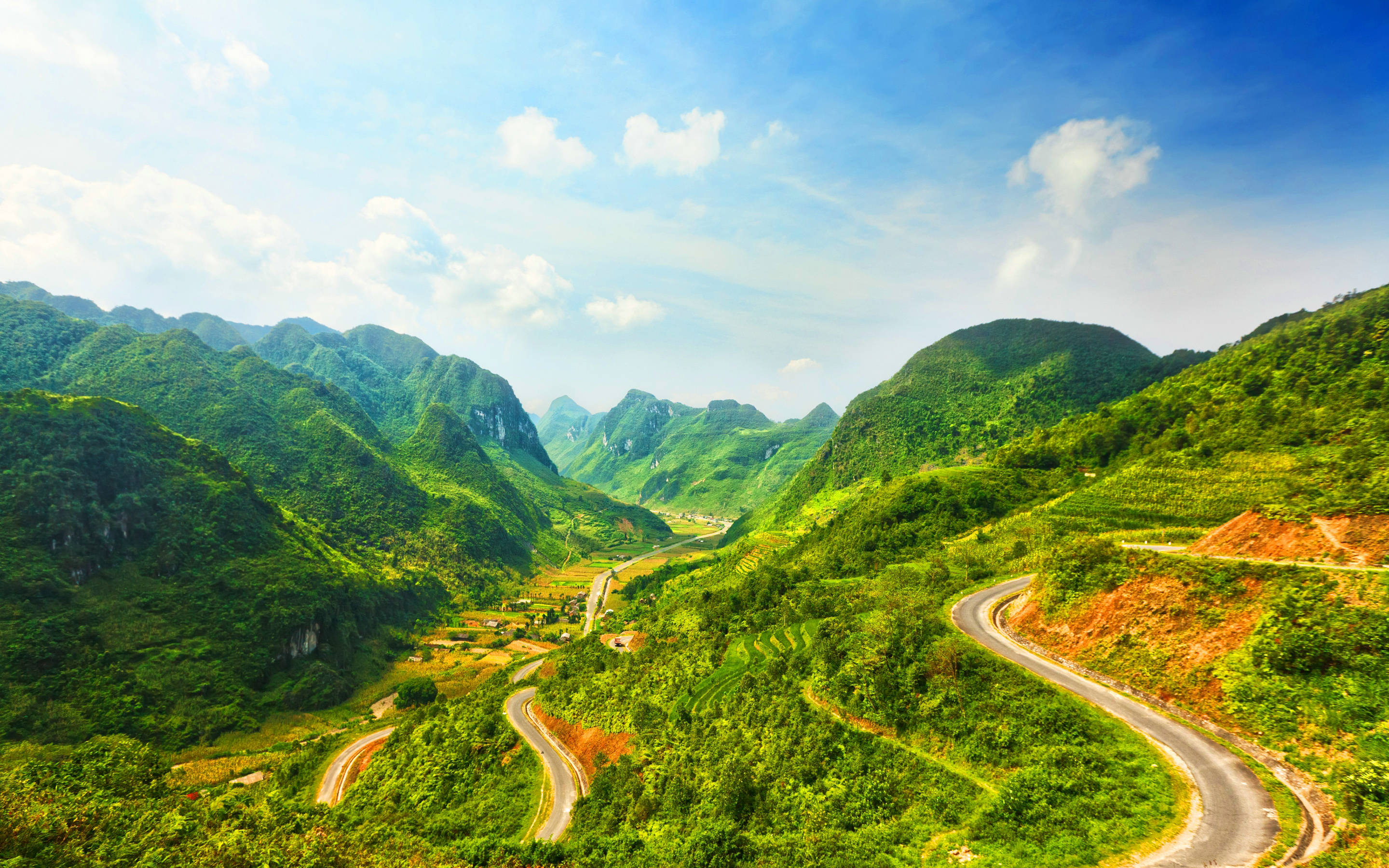 越南考帕山口 壁紙 — 一條蜿蜒的瀝青公路在明亮的藍天白雲下，蜿蜒穿過鬱鬱蔥蔥的青山。