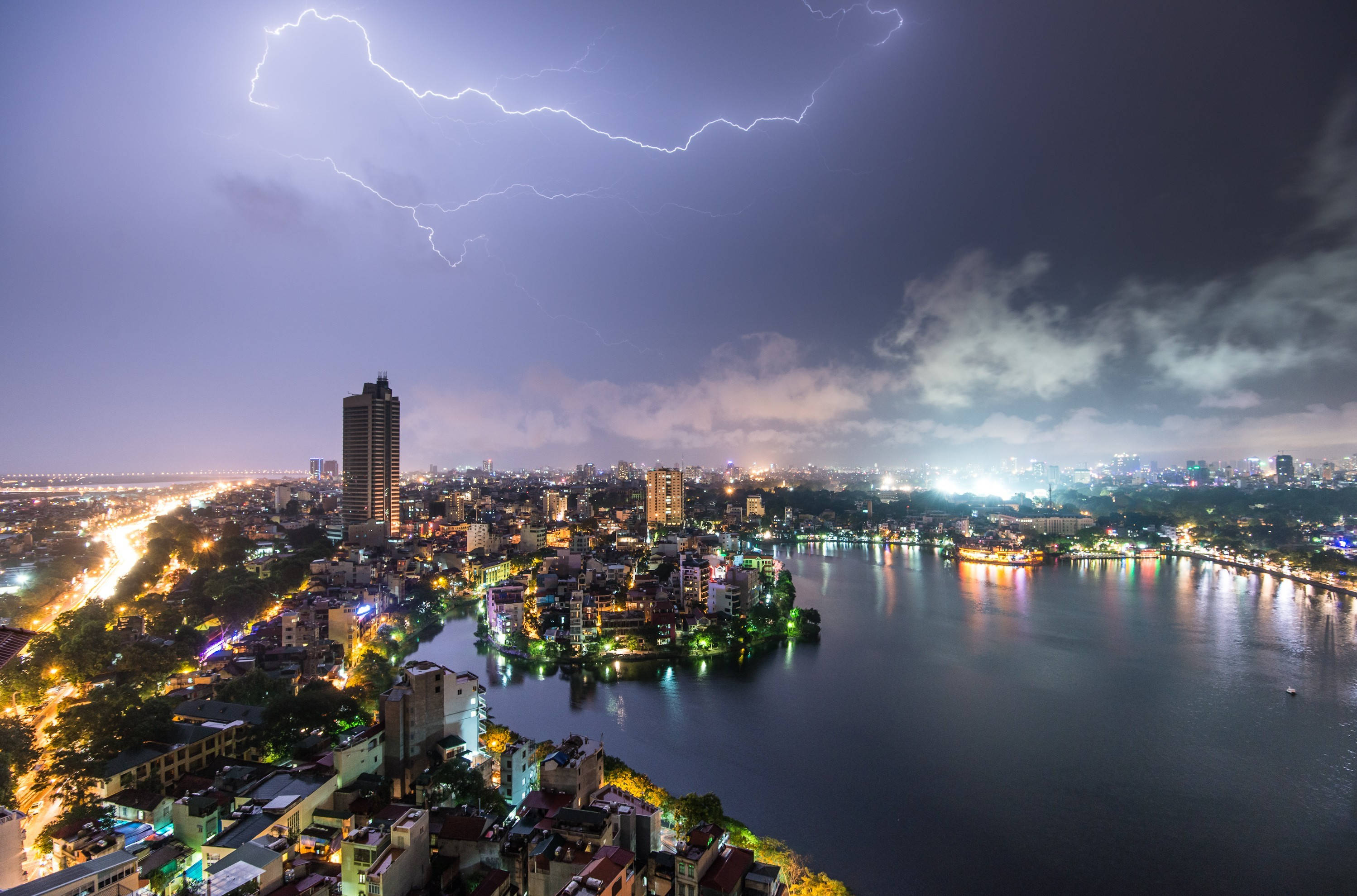 越南雷暴城市 壁紙 — 一幅戲劇性的夜景城市景觀，巨大的閃電照亮了閃爍的城市海濱上空。