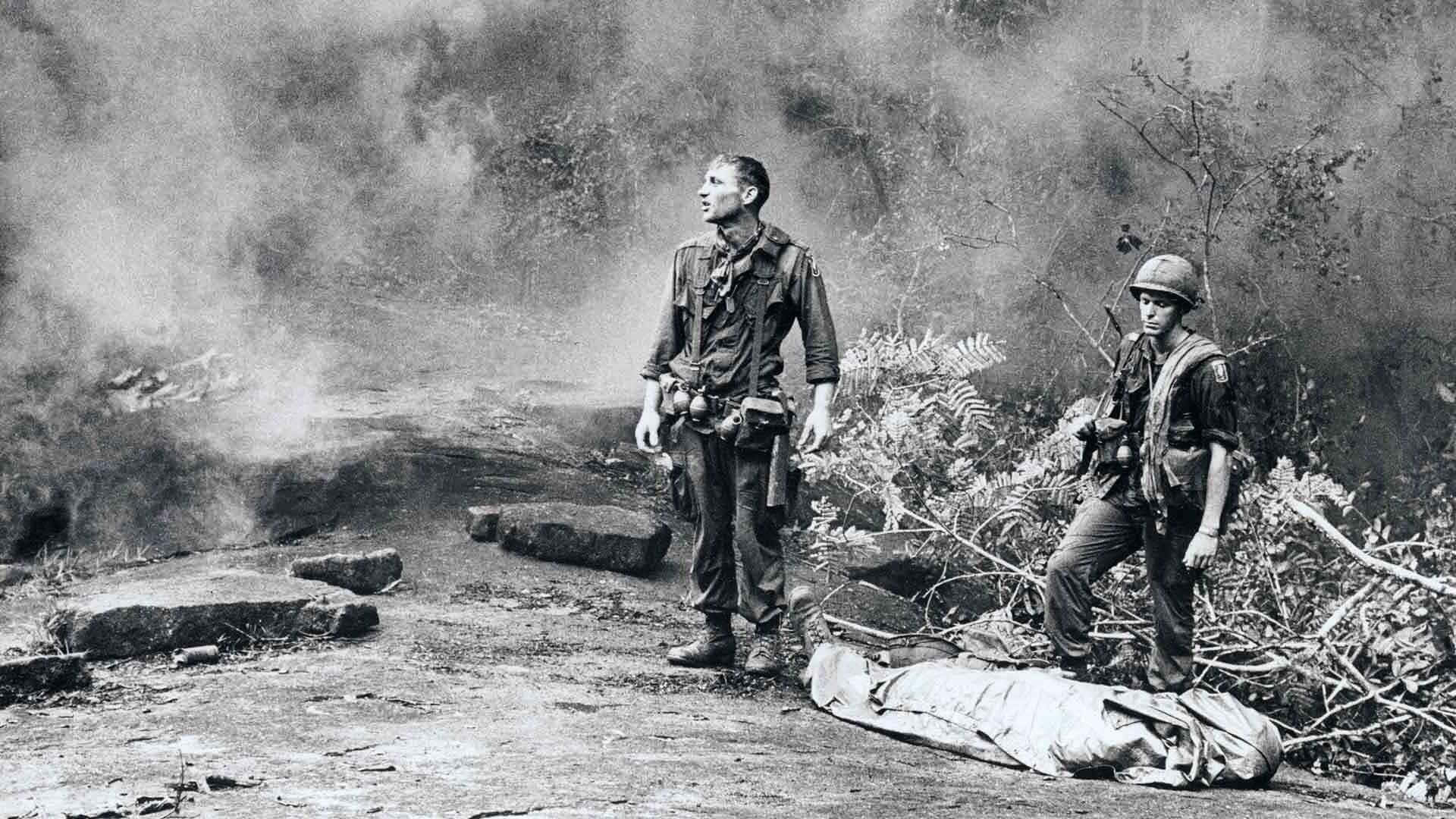 兩名身穿叢林裝備的士兵在戰鬥後站在用防水布包裹的屍體附近。