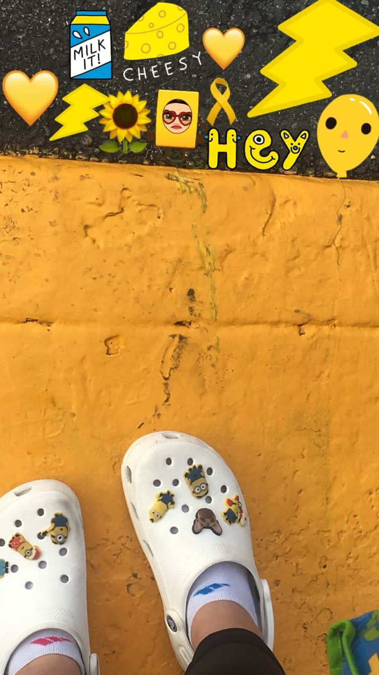 趣味繽紛的Crocs 壁紙 — 白色Crocs鞋搭配Minion吊飾，立於亮黃色牆壁旁，旁邊是覆蓋著俏皮黃色貼紙的黑色表面。