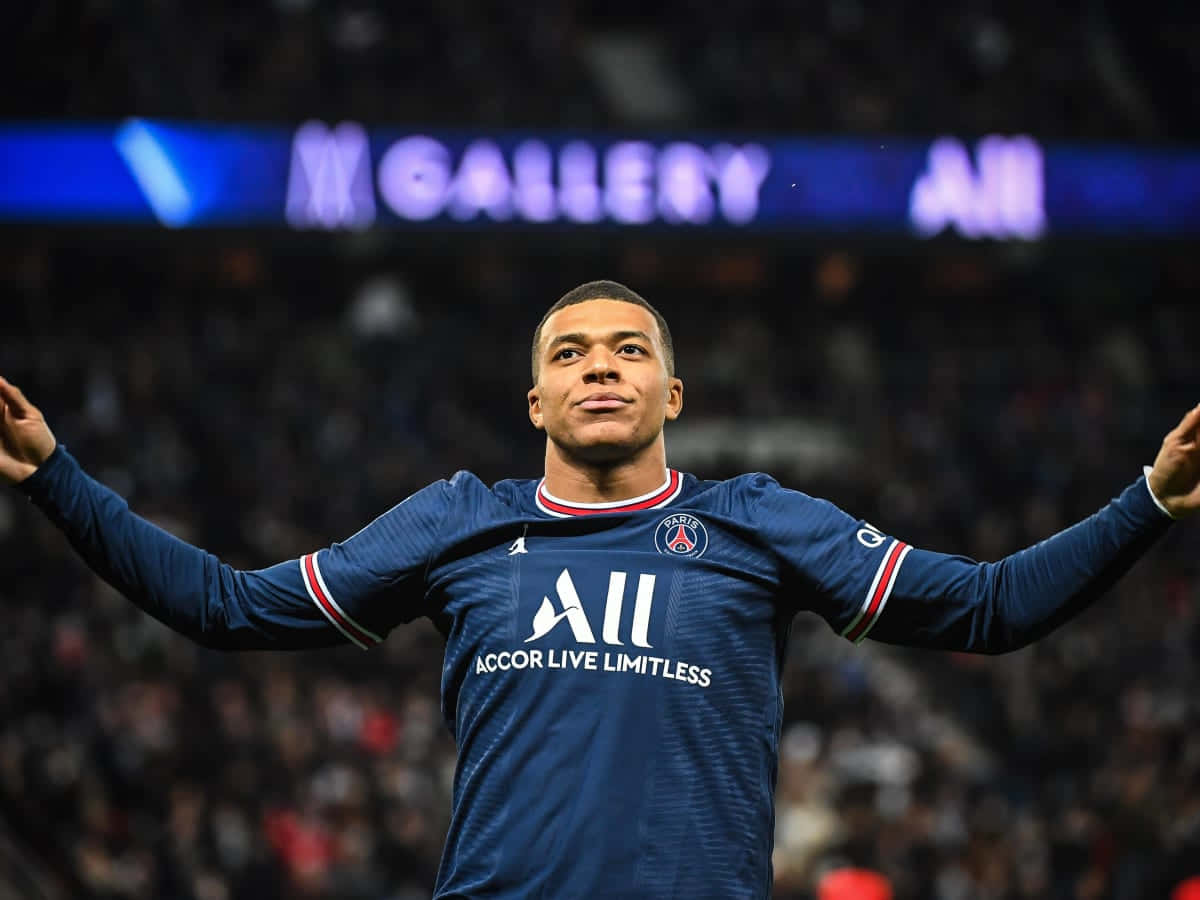 Mbappe 桌布 壁紙 — 足球員基利安·麥巴比在球場燈光下身穿藍色PSG球衣，張開雙臂勝利慶祝。