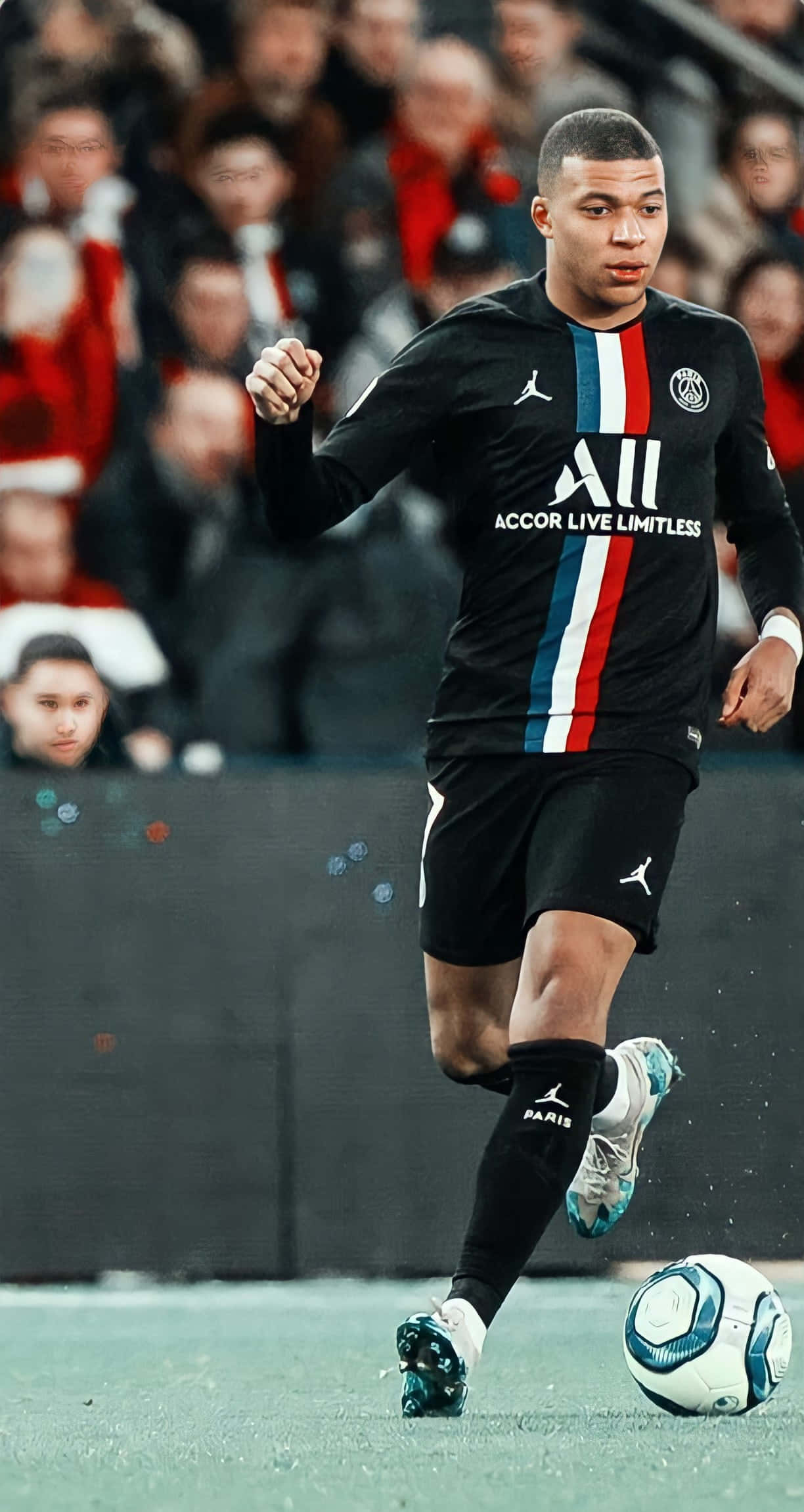 Mbappe 桌布 壁紙 — 足球員基利安·麥巴比在綠色球場上盤球，背景是模糊的體育場觀眾。