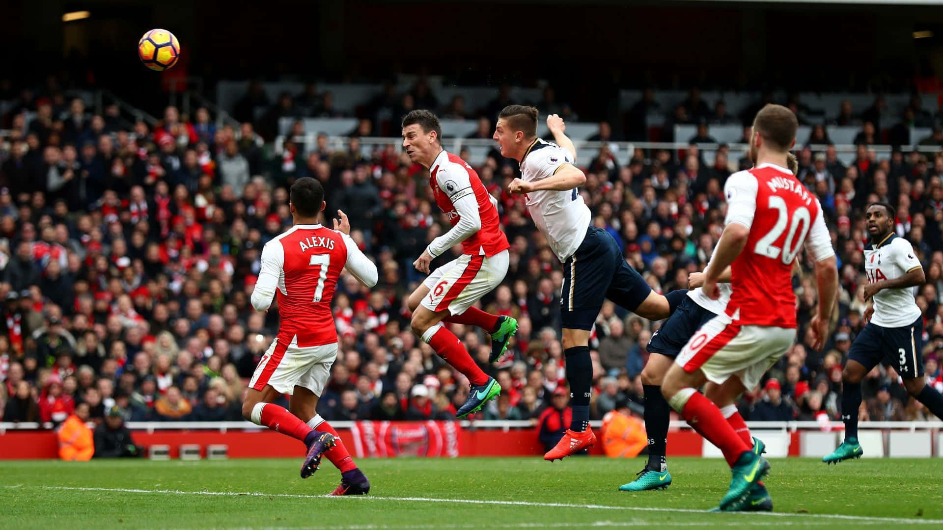 Arsenal 桌布 壁紙 — 足球運動員在擠滿觀眾的體育場內，於一場高風險比賽中跳起爭球。