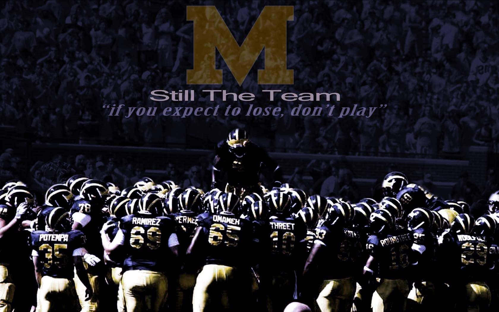 Michigan Wolverines 桌布 壁紙 — 足球隊在體育場人群中聚集在一個巨大的金色M字下，並帶有勵志語錄。