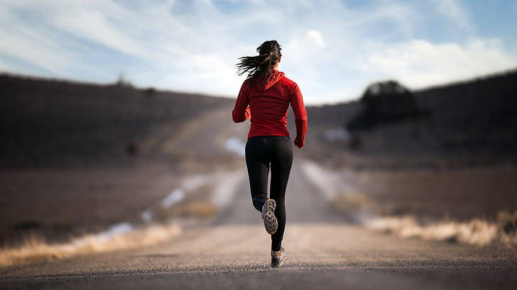 跑步女孩運動 4K 壁紙 — 一位身穿紅色連帽衫的女子在晴朗藍天與薄雲下，獨自奔跑在塵土飛揚的鄉村道路上。